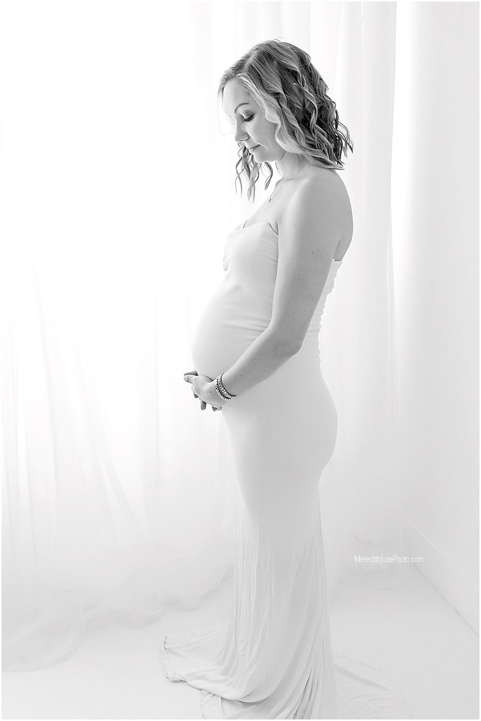 A series of ethereal black and white maternity photos showing a pregnant woman in a flowing white dress by sheer curtains.