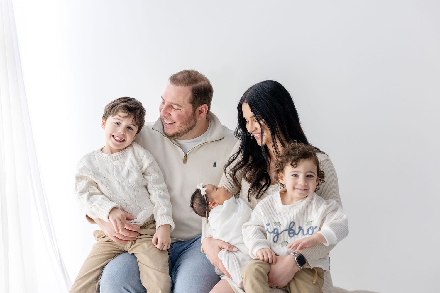 A family wearing neutral colored clothing poses together on a white background for a series of casual portraits.