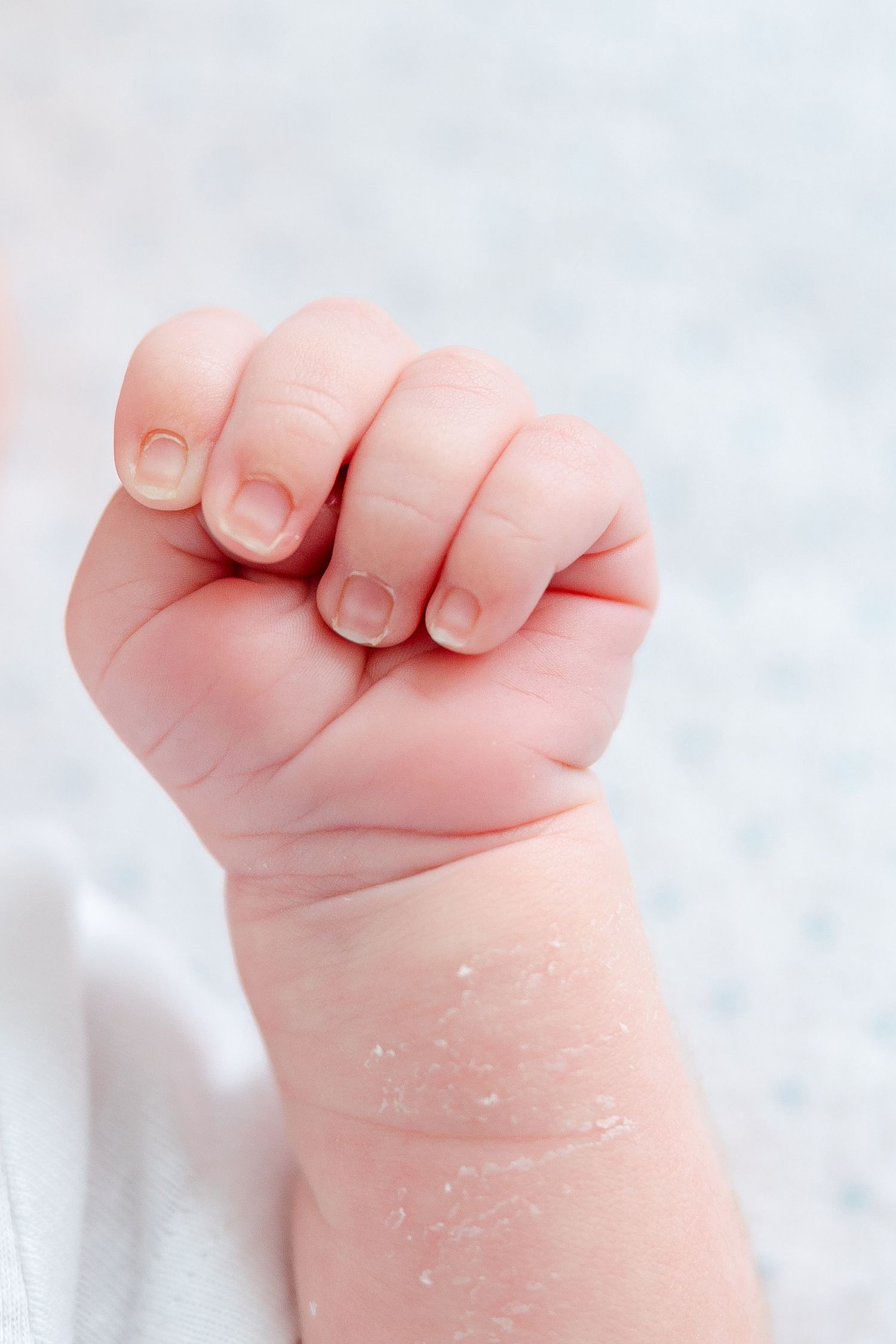 Close-up sequence of a tiny baby's hand curled into a delicate fist against a soft white background.