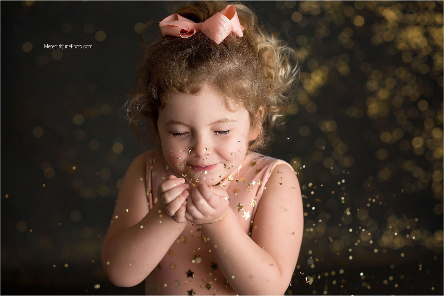 Child with curly hair laughs while glitter sparkles fall around them in a magical outdoor portrait session.