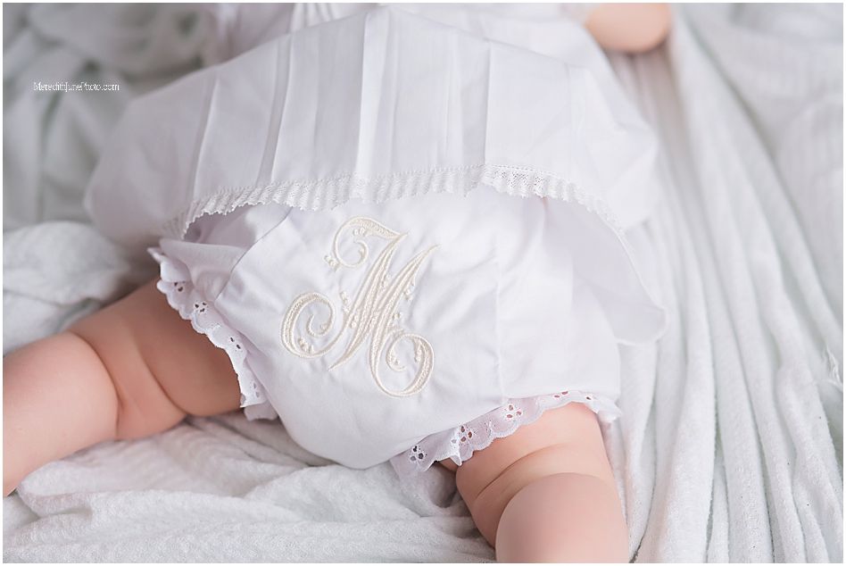 Close-up of a white monogrammed baby dress with delicate lace trim laying on soft fabric.