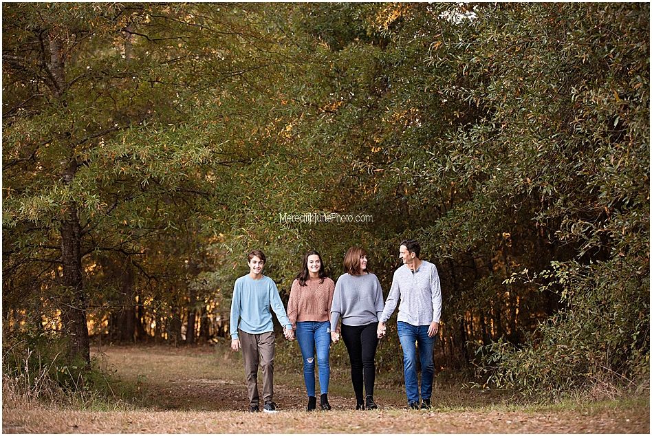 A group walks together on a leaf-covered trail through autumn trees on a sunny afternoon.