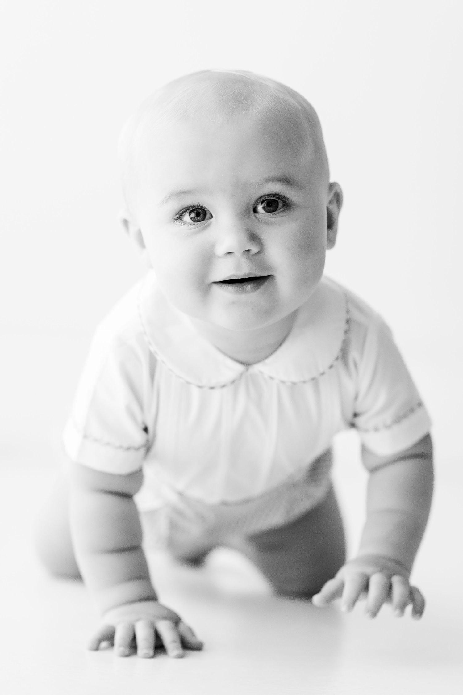 Baby in white clothing crawls and poses on white background.
