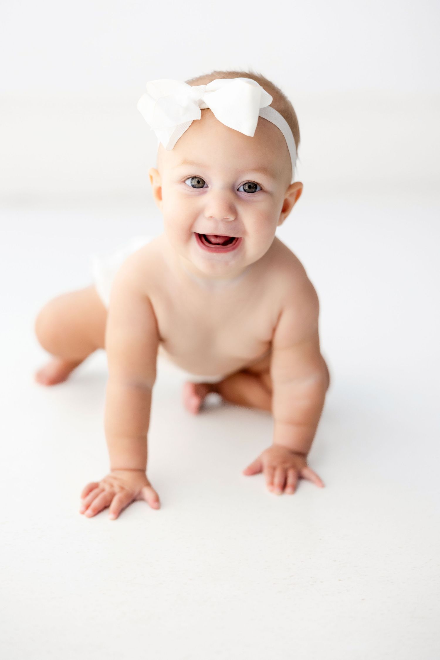Baby wearing white bow headband crawls on white background in series of adorable poses.