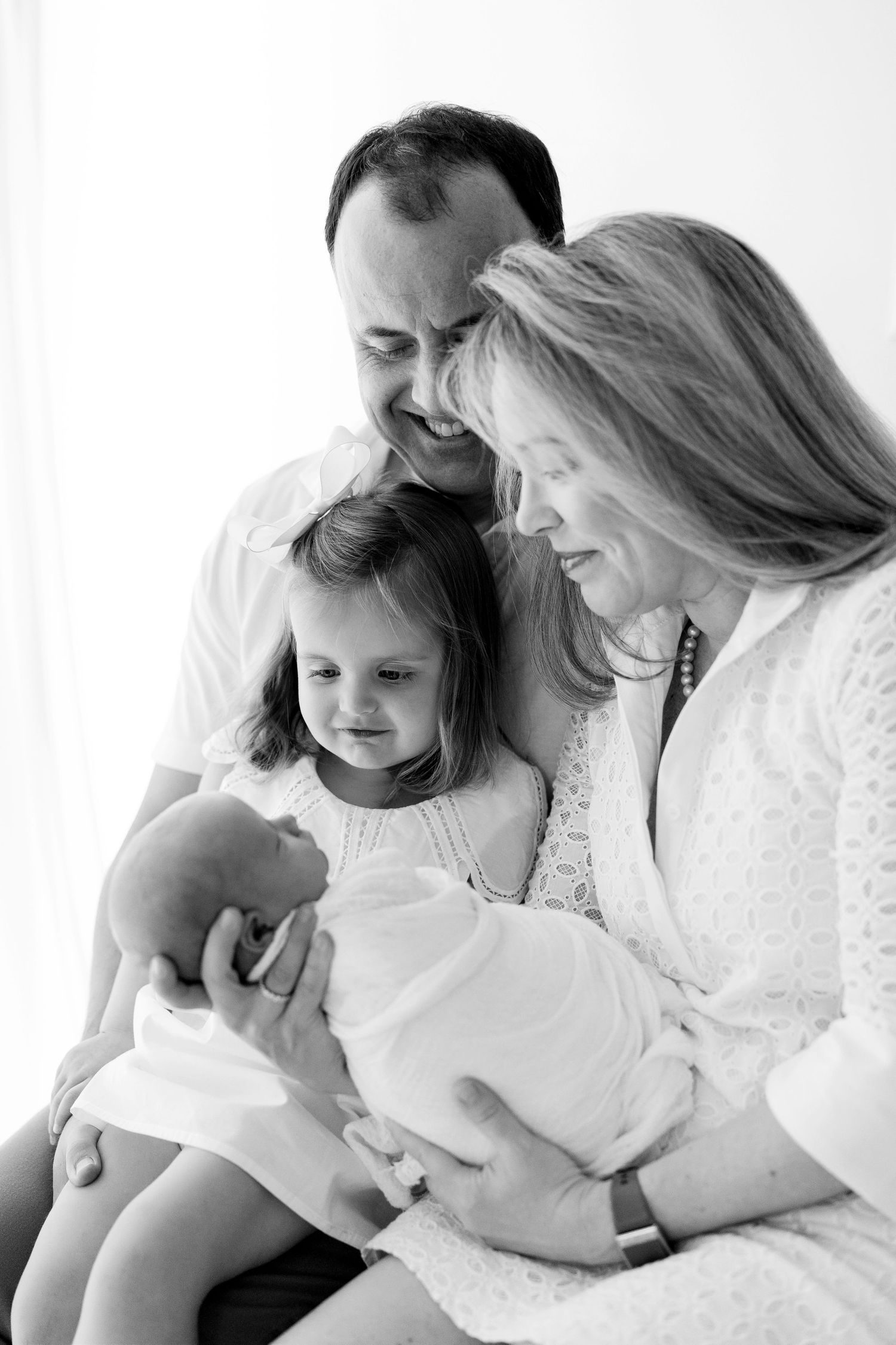Happy family of four admiring their newborn baby in black and white studio portrait photo.