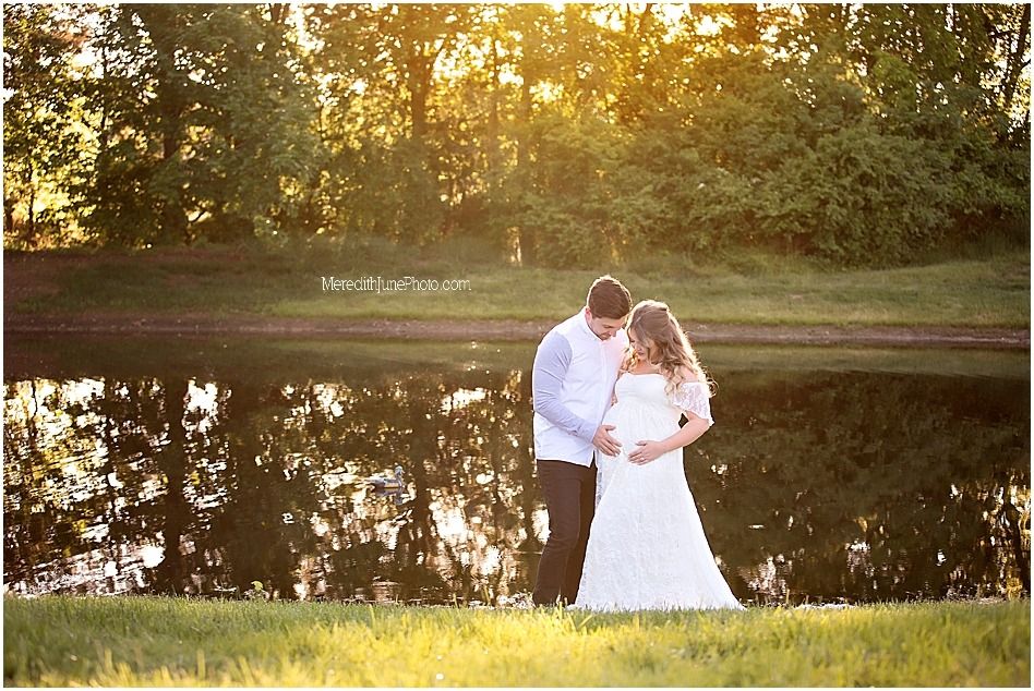 A couple in white outfits embraces during a romantic sunset photoshoot in a grassy field.
