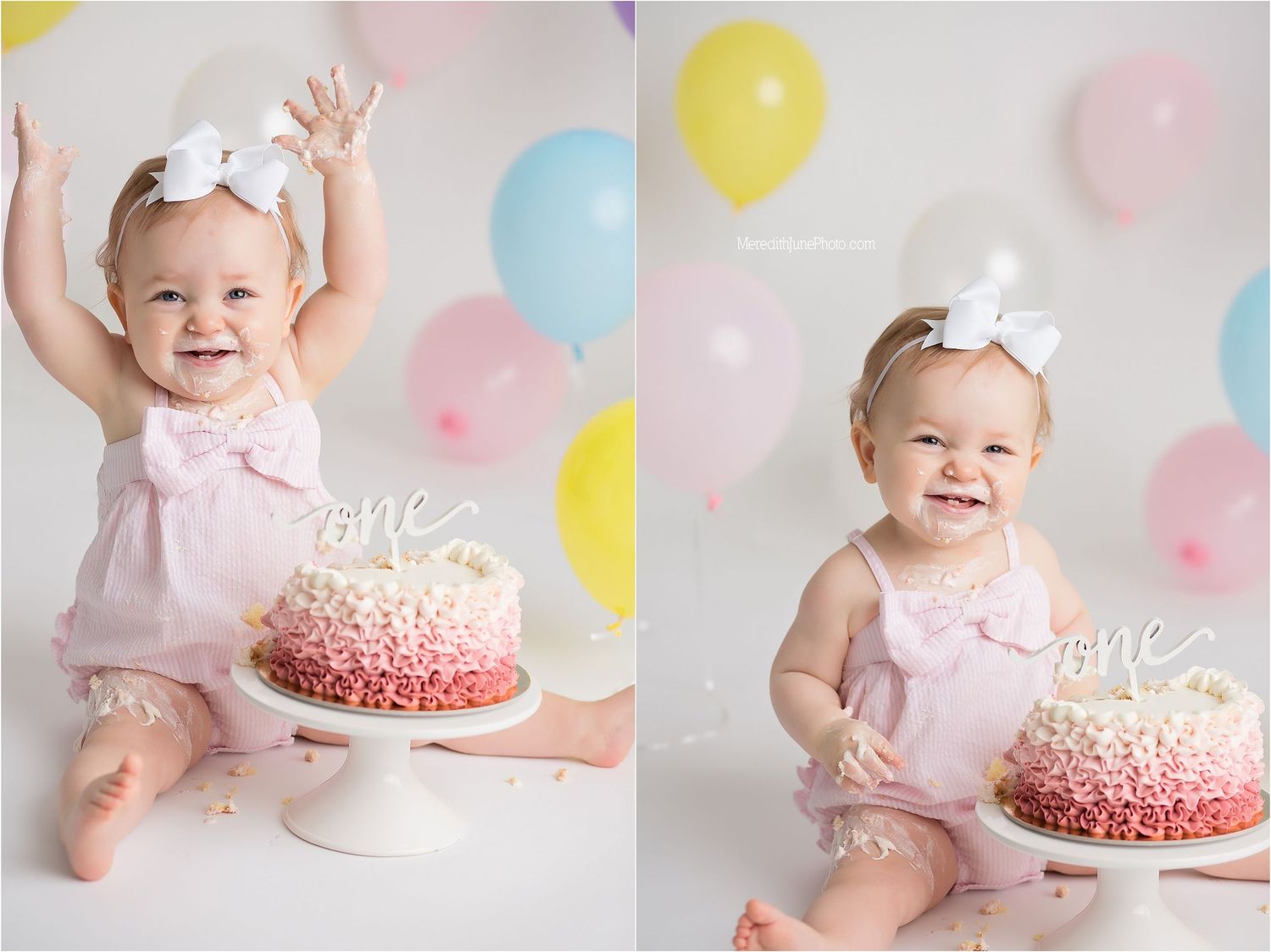 Baby in pink dress sits next to pink and white smash cake with balloons in background for first birthday celebration.