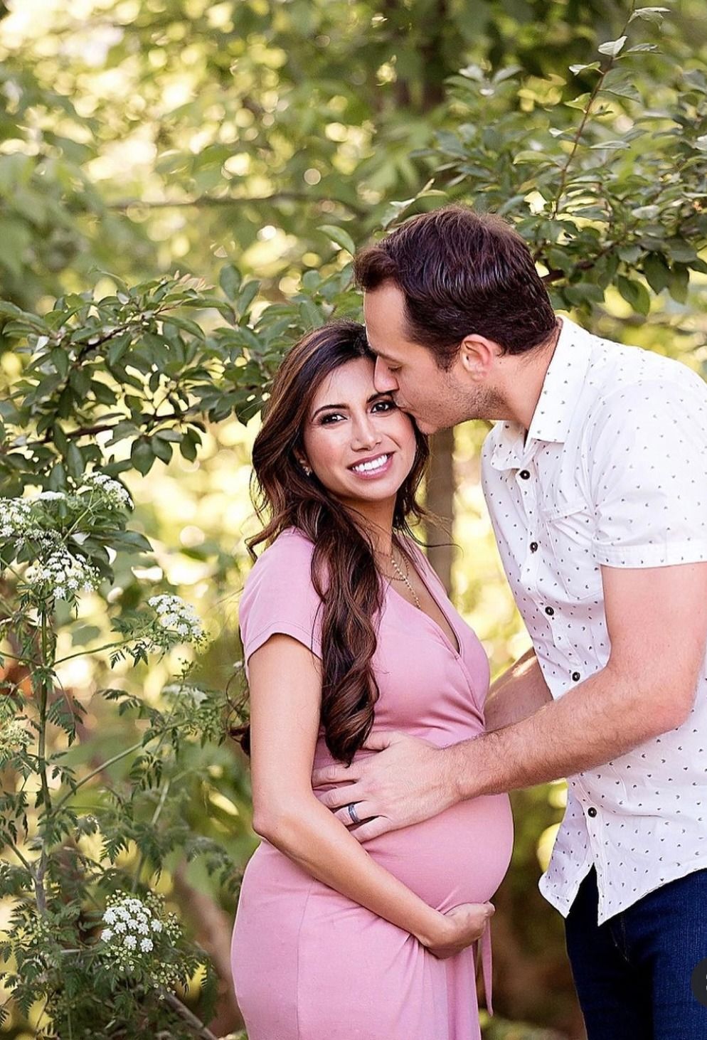 A couple shares an intimate moment outdoors in a garden setting with soft natural lighting and greenery.