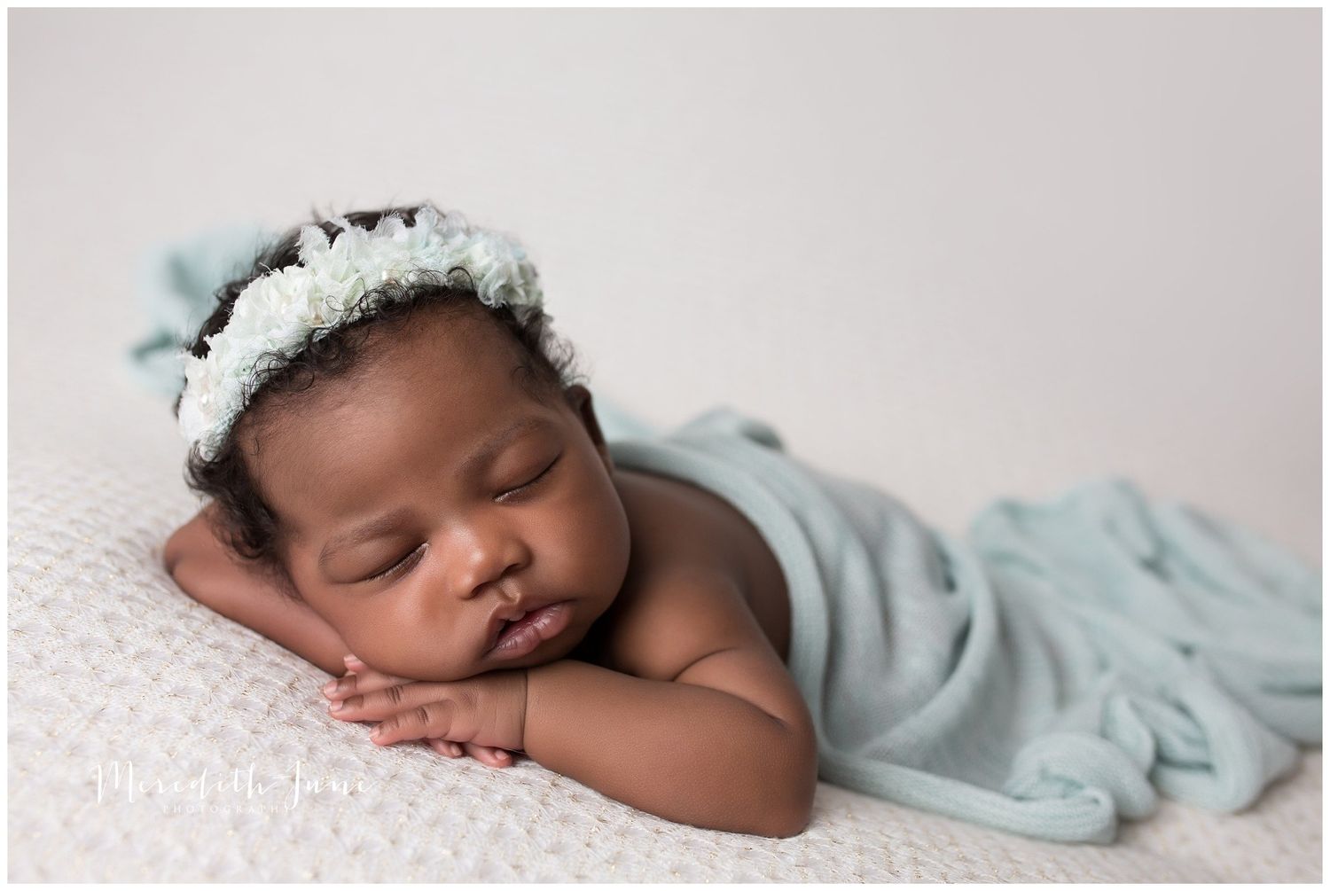 Sleeping baby wrapped in soft mint green blanket lying on white surface with peaceful expression.