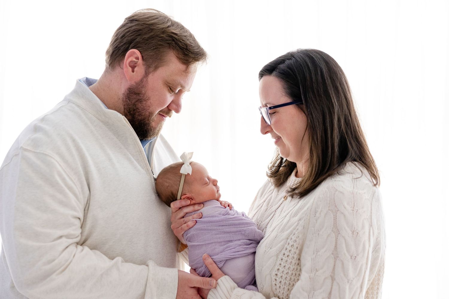 Parents in white shirts share tender moments with their newborn baby in a series of intimate family photos.