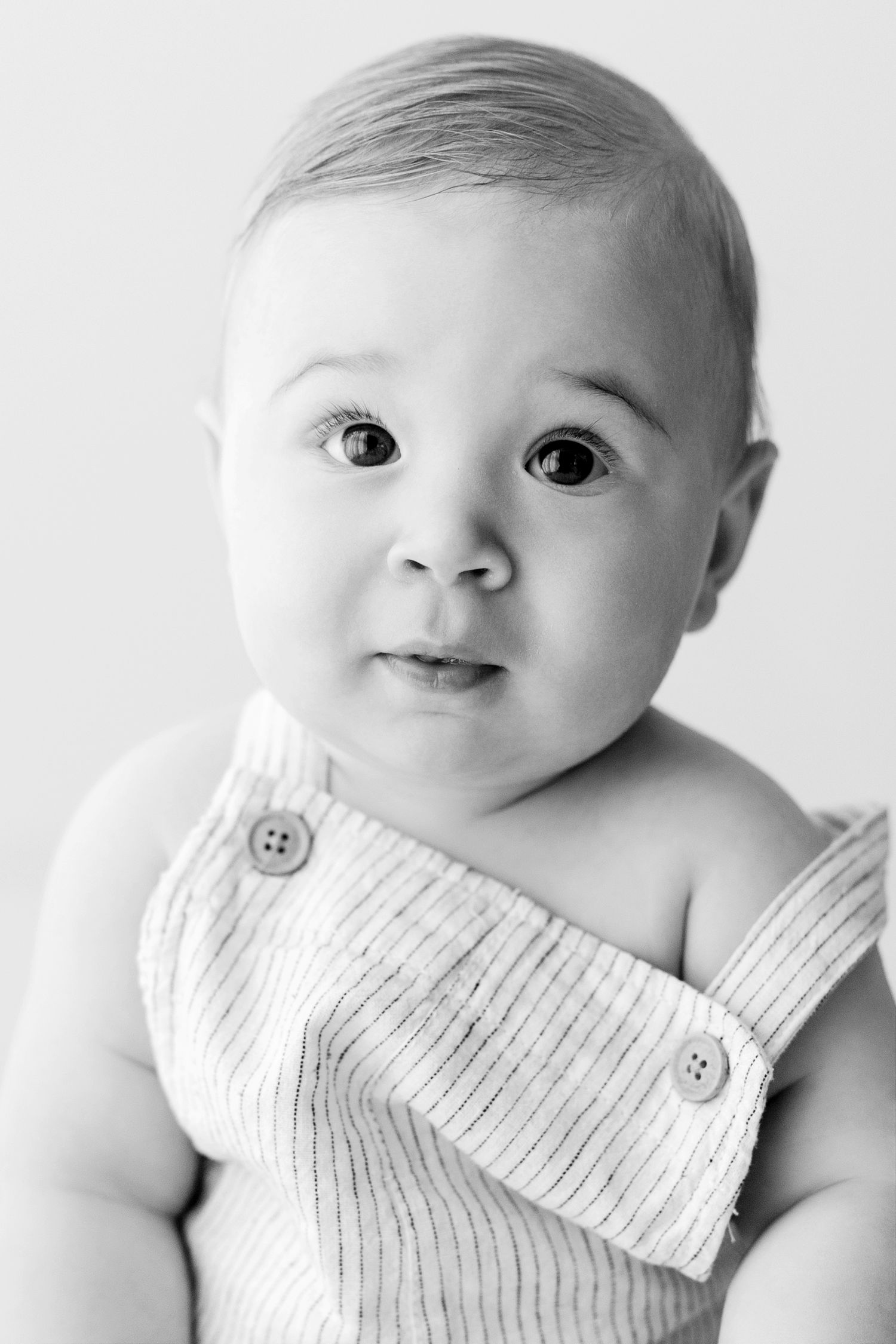 Black and white portrait of a baby wearing a white ribbed romper with buttons.