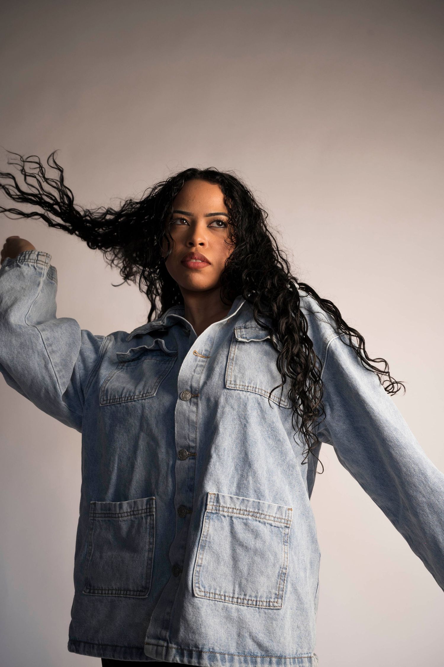 A fashion editorial series showing a denim jacket against a light background with dynamic movement and flowing hair.