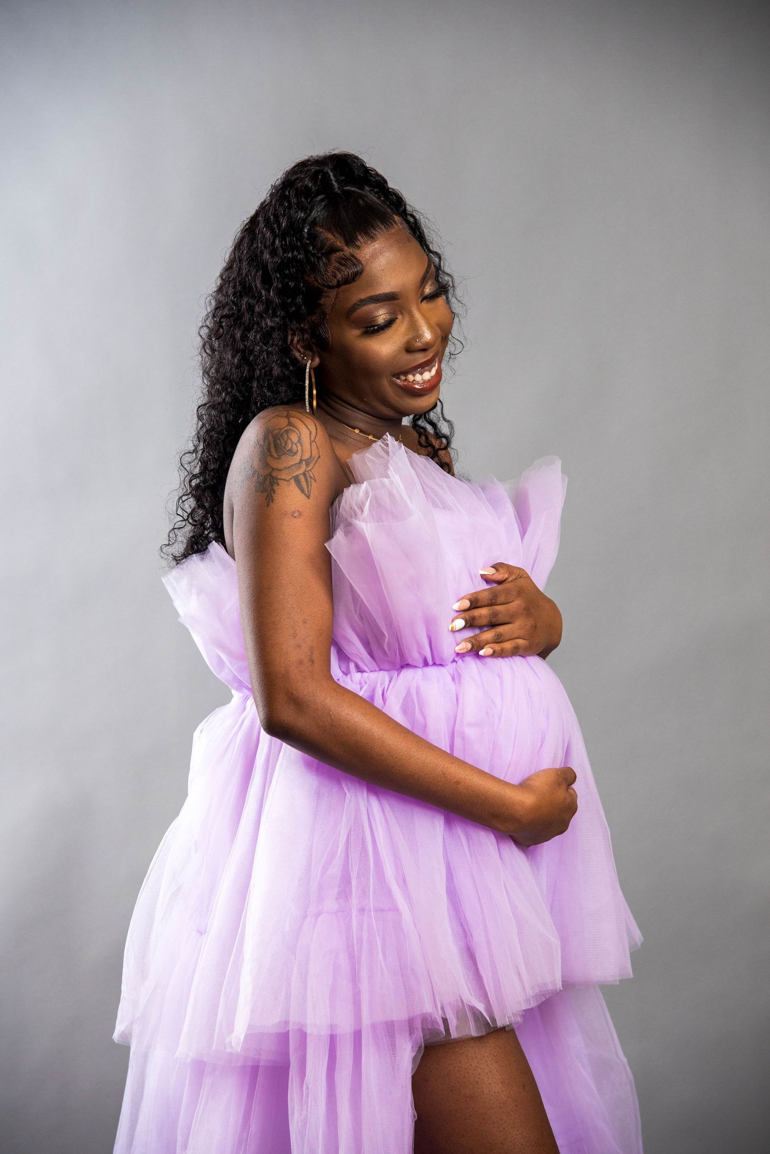 A maternity photo featuring a flowing pink tulle dress against a grey backdrop.