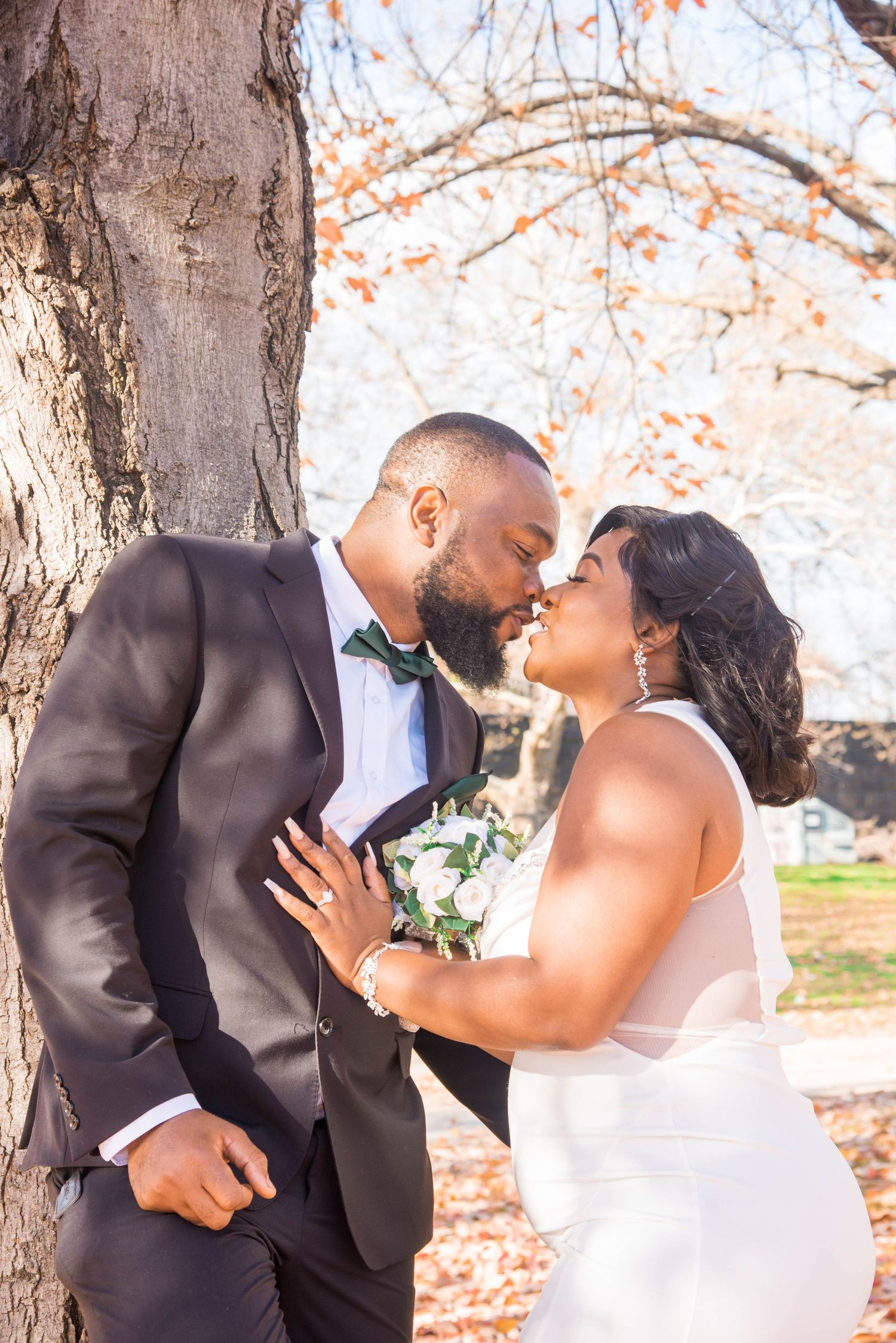 Romantic wedding photo of couple under autumn tree with white dress and black tuxedo.
