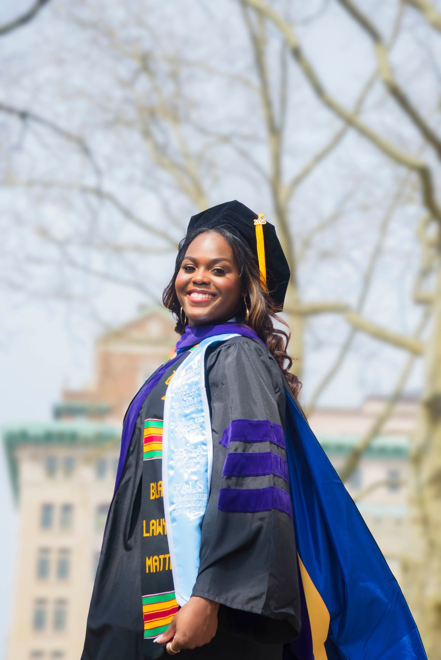 Graduate in academic regalia smiling outdoors during graduation photoshoot.