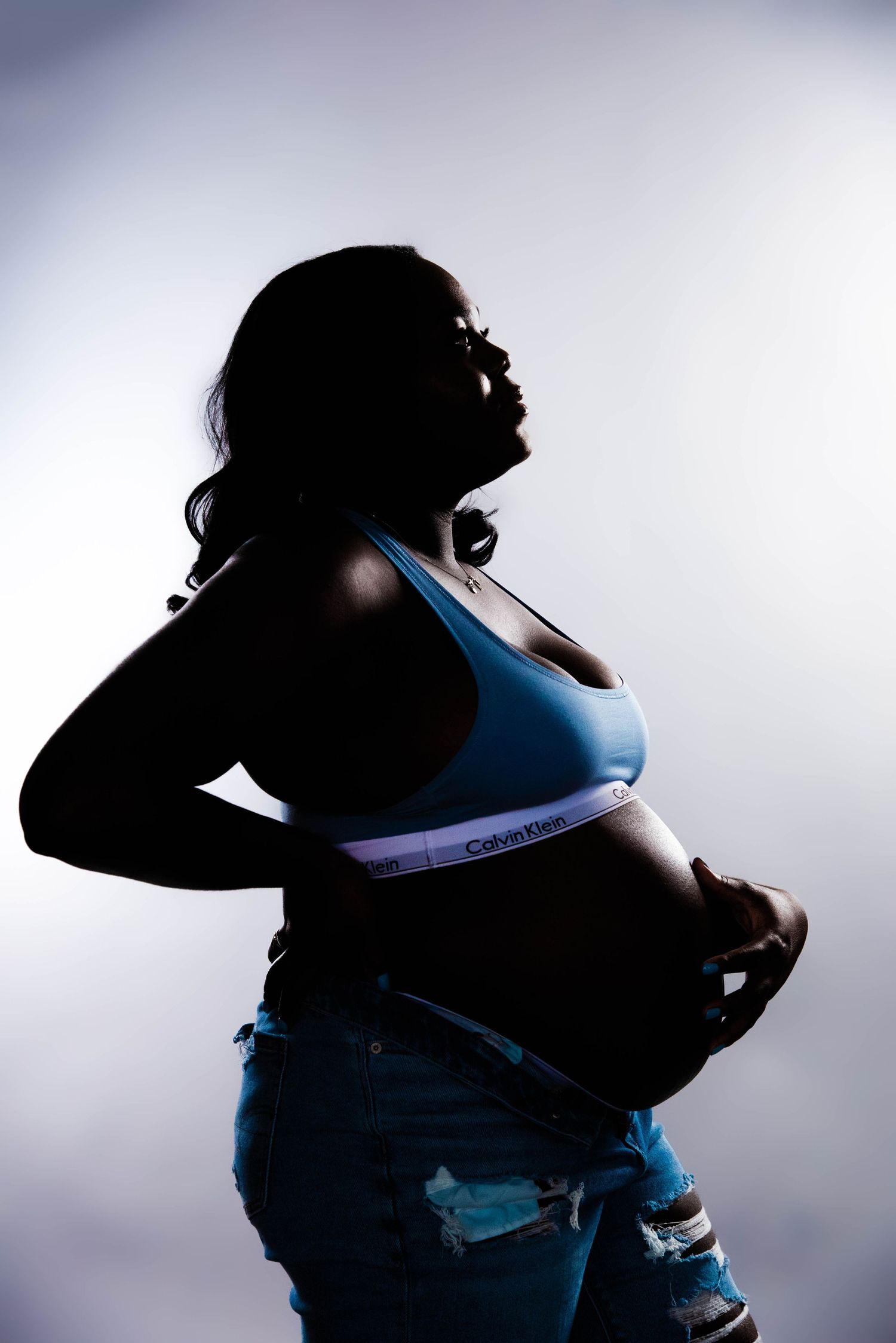 A dramatic silhouette of a pregnant woman in athletic wear against moody lighting.