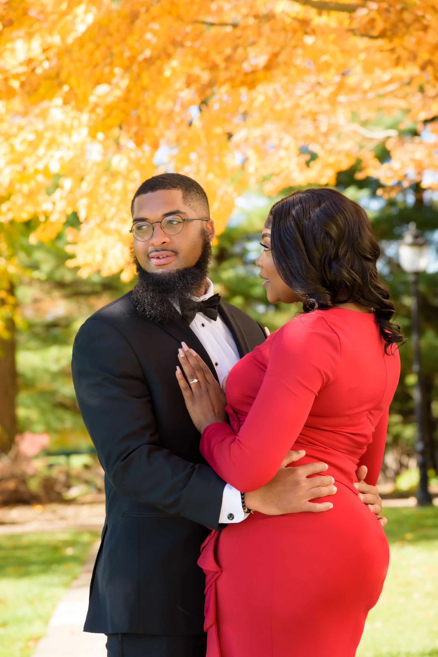 Elegant couple in formal wear embracing under golden autumn foliage.