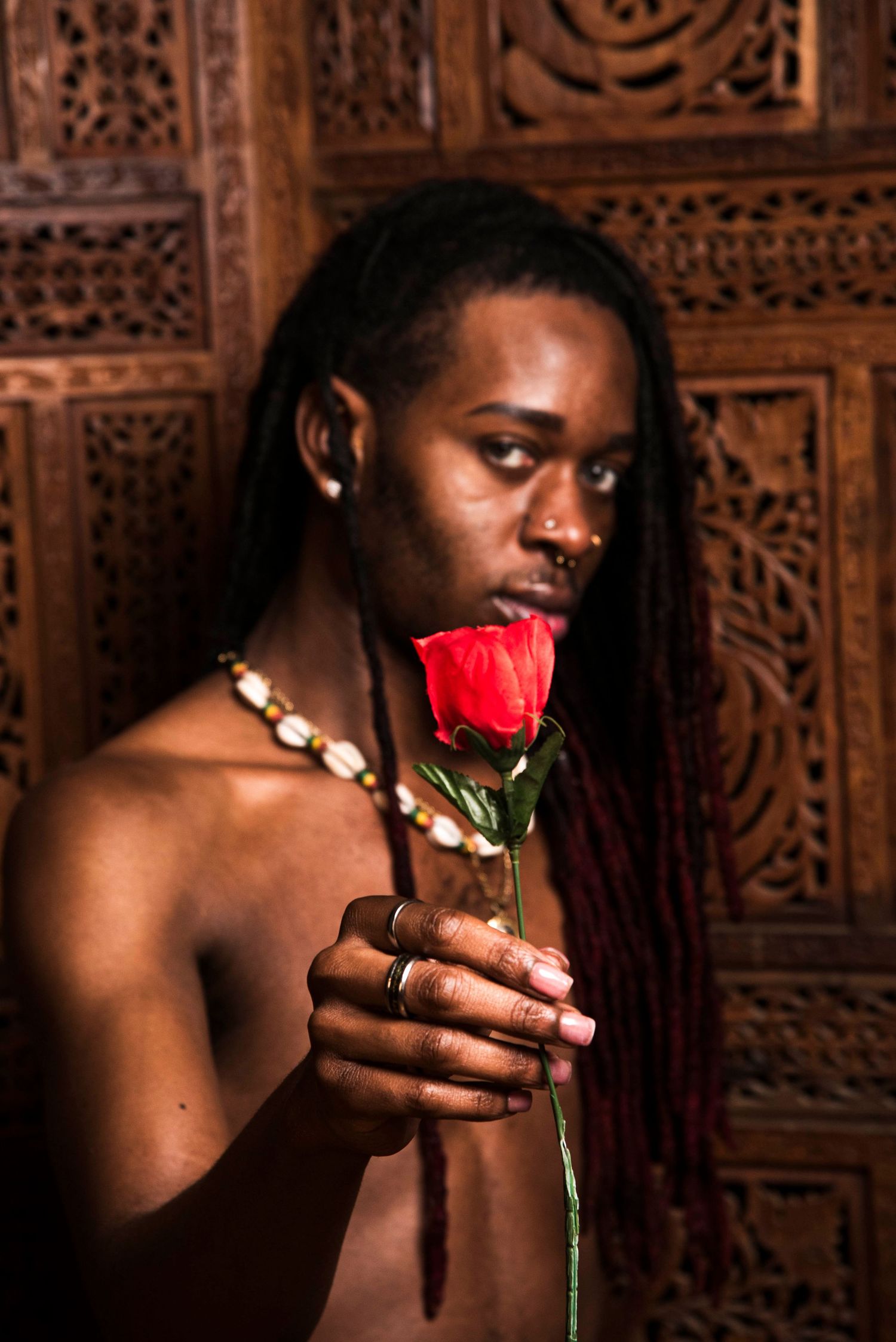 Artistic portrait with red rose against ornate wooden carved background.