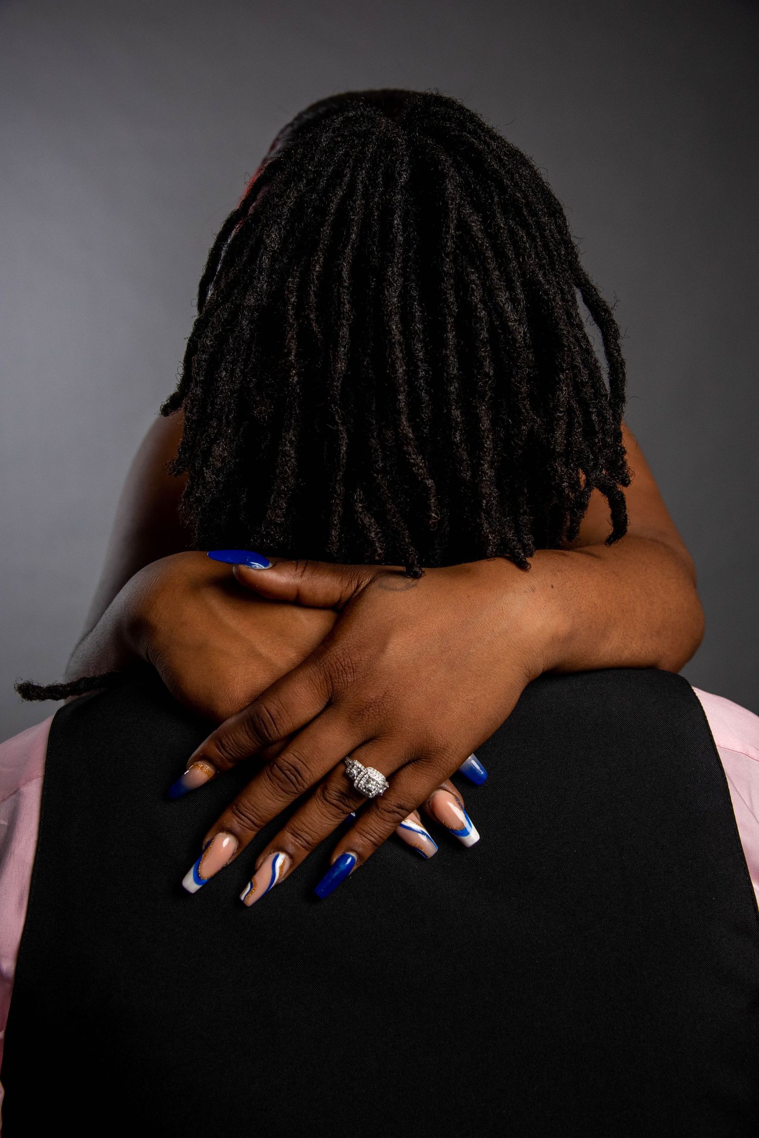 Close-up of dreadlocks and blue manicured nails with engagement ring against dark background.