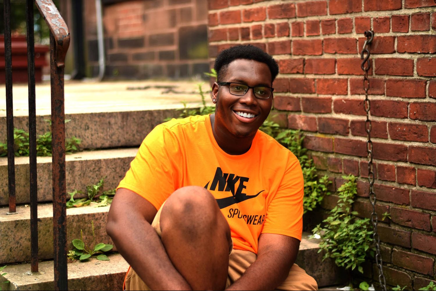 Person in bright orange Nike shirt sitting on brick steps outdoors.