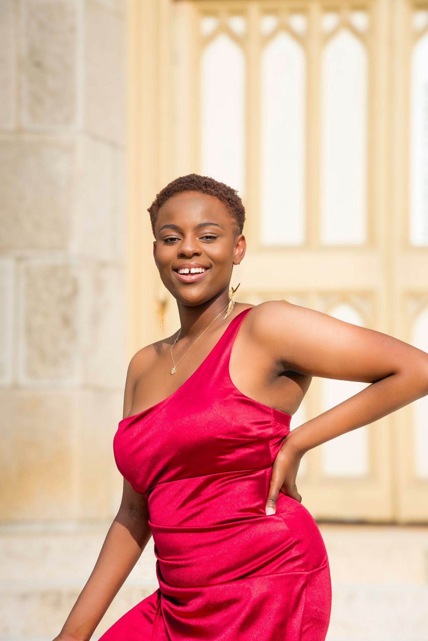 Dynamic poses in red formal dress against architectural backdrop with arched windows.