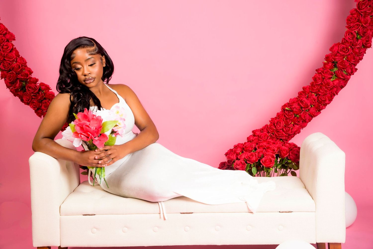 Person in white dress reclining on white couch with red floral backdrop.