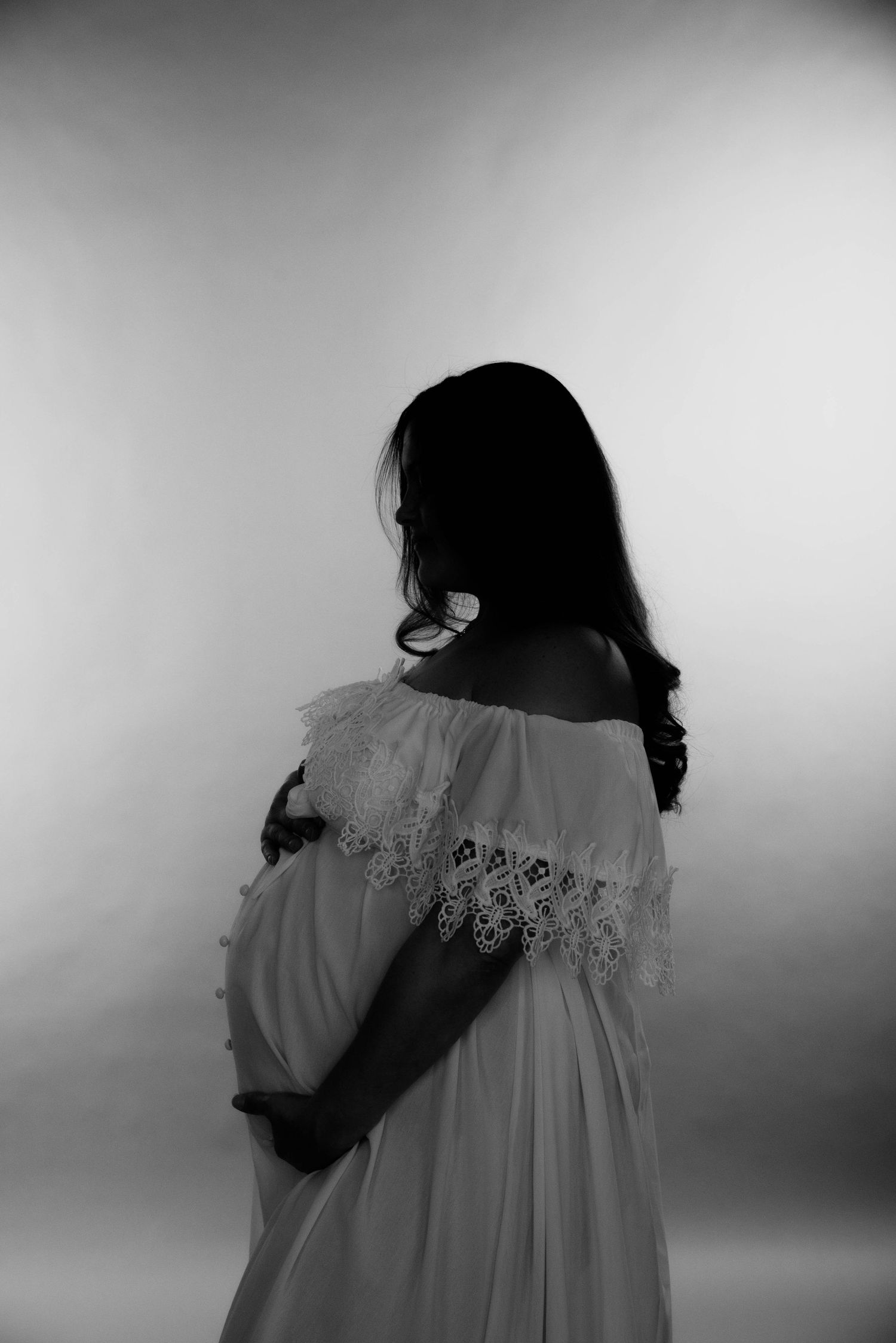 A silhouette maternity photo showing a pregnant woman in a lace dress against a light background.