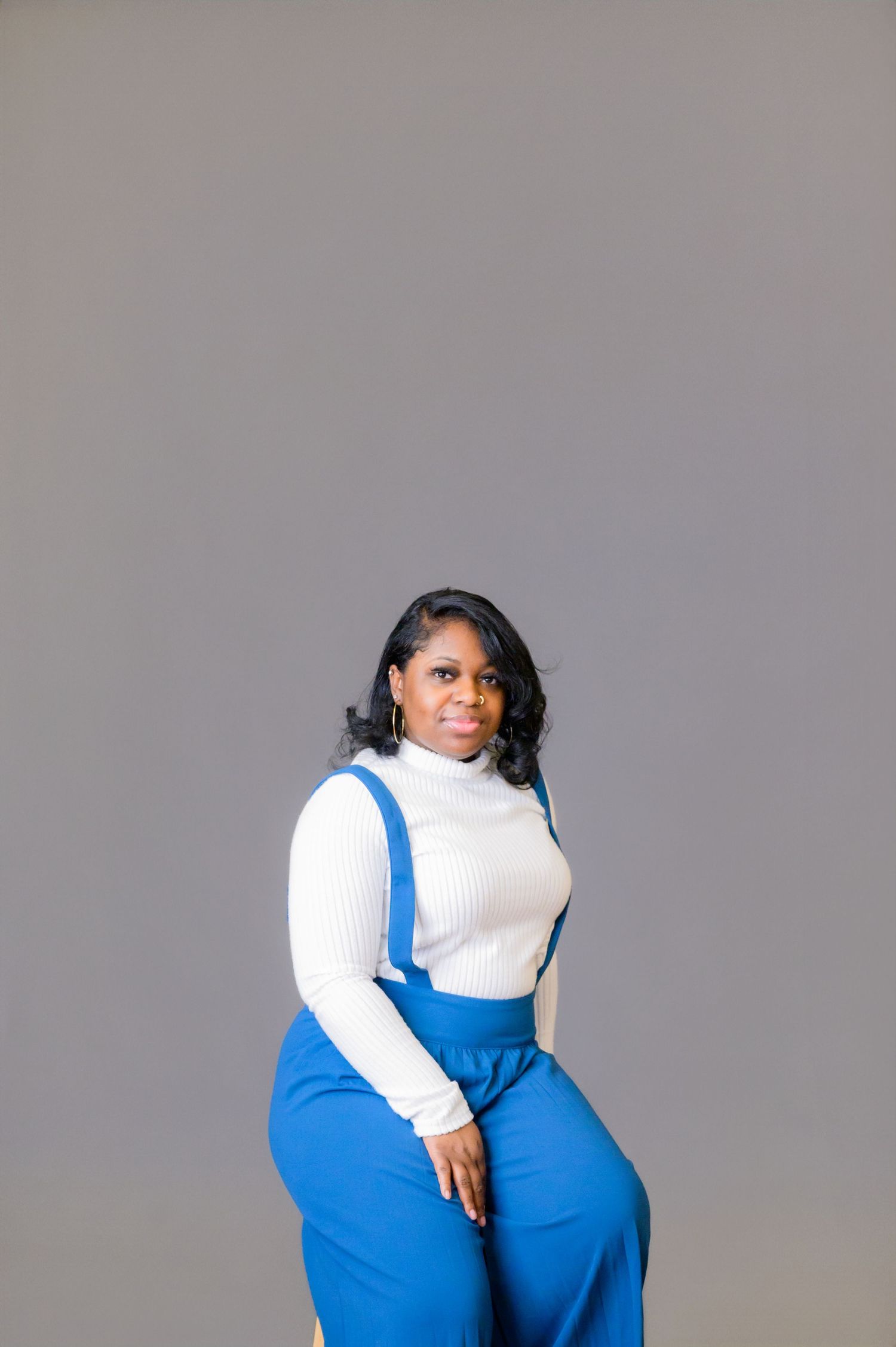 Model wearing bright blue overalls and white sweater poses artistically in studio setting.
