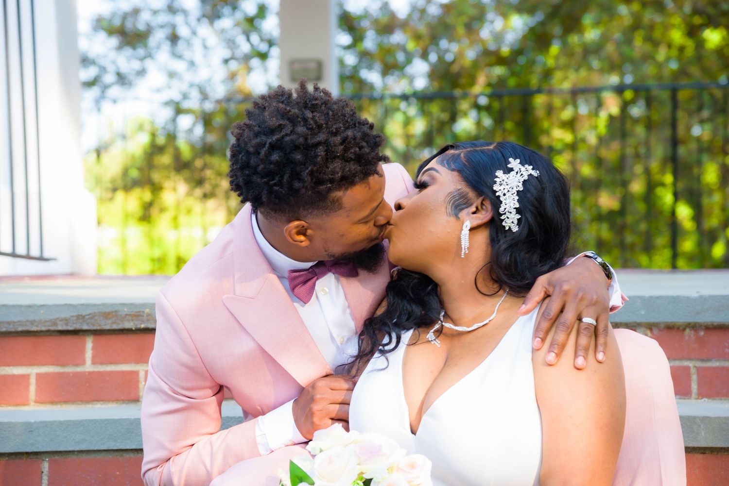 Intimate wedding portrait of couple kissing on brick steps in sunlit garden setting.