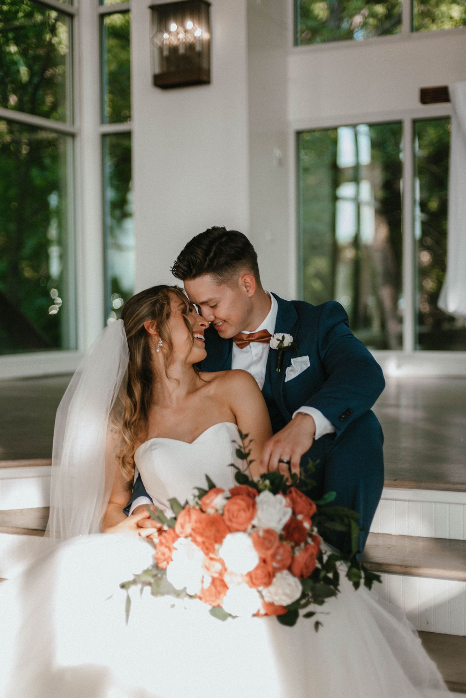 Romantic wedding couple shares intimate moments on white couch with coral floral arrangements.