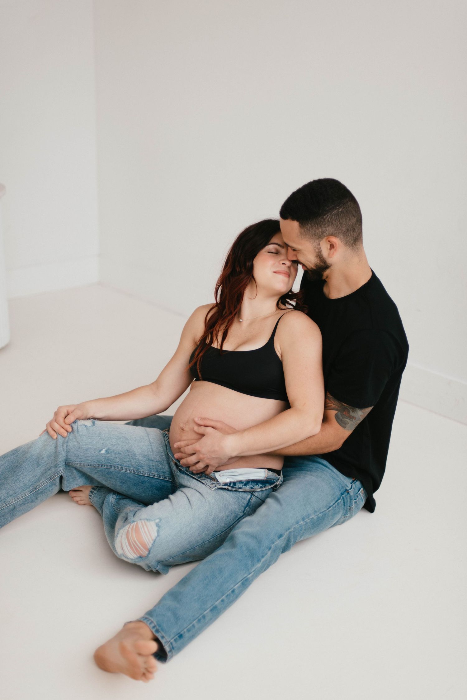 Couple in casual attire lounging intimately on white floor.