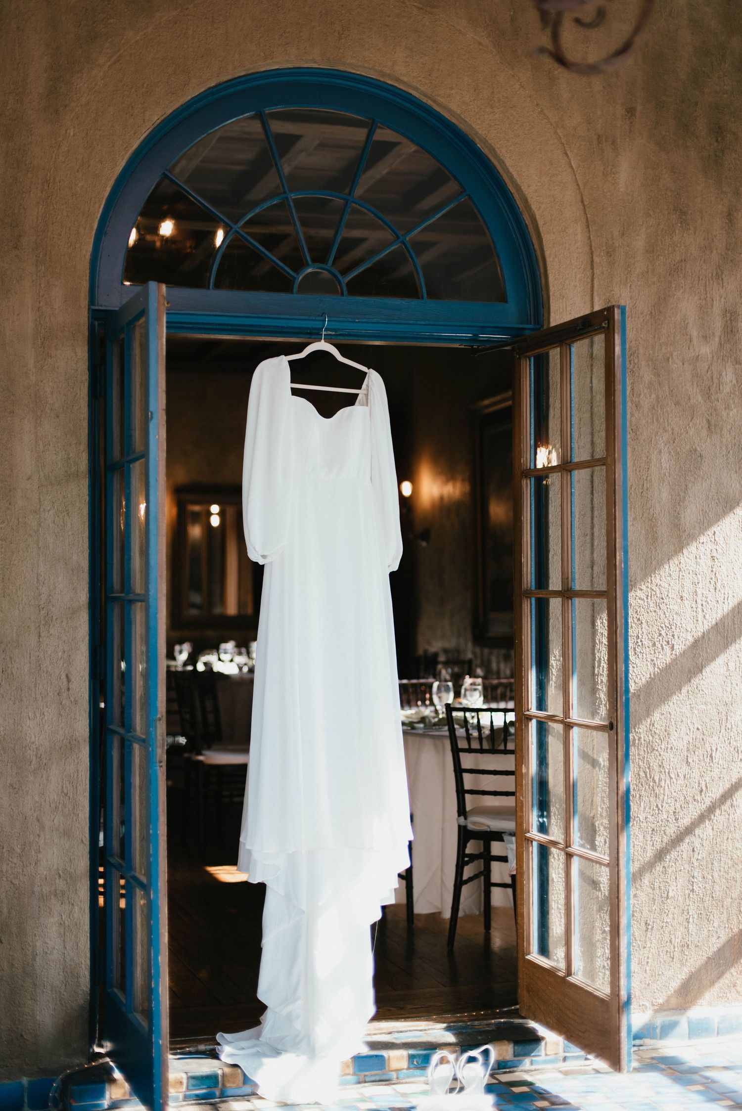 White wedding dress hanging in a rustic doorway with blue trim and natural lighting.