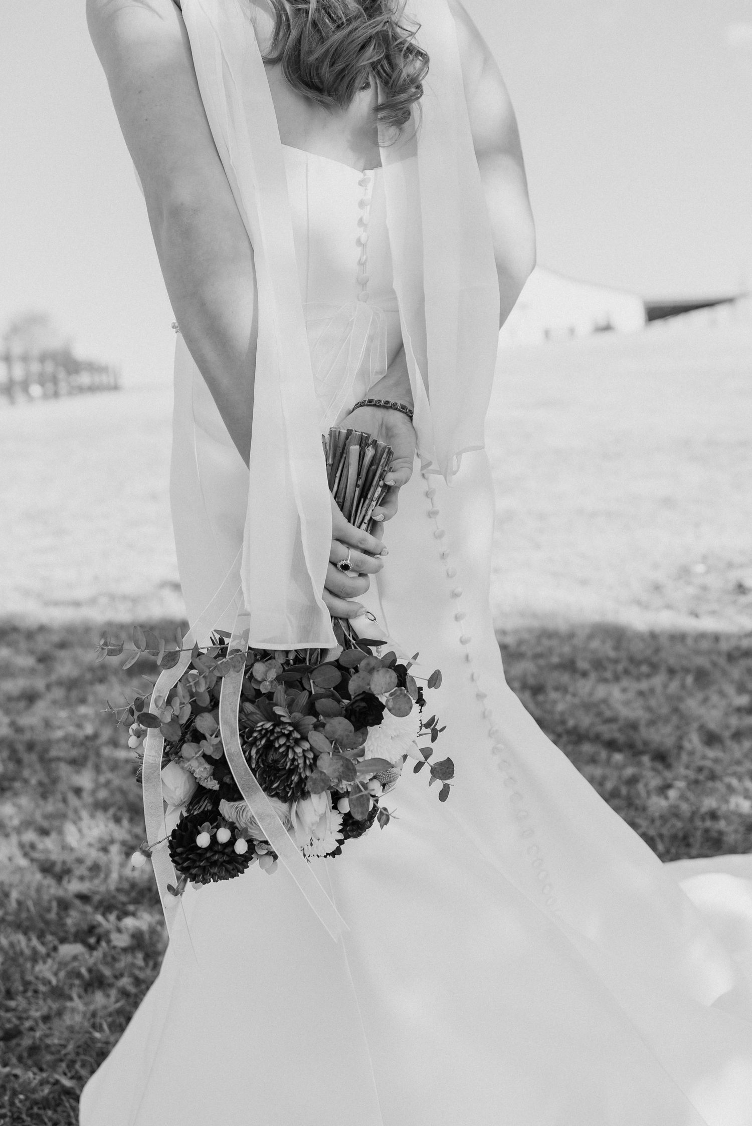 Detail shot of bride's wedding dress and bouquet against outdoor setting in black and white.