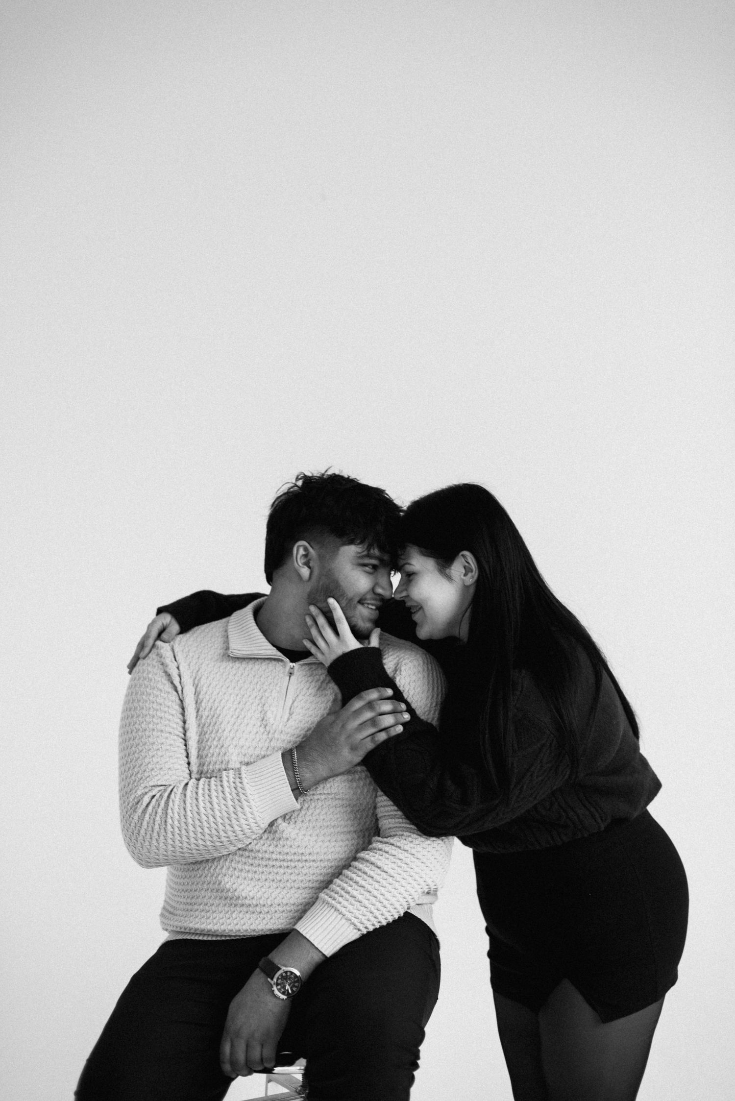 Couple in casual attire shares intimate black and white portrait moments against white backdrop.