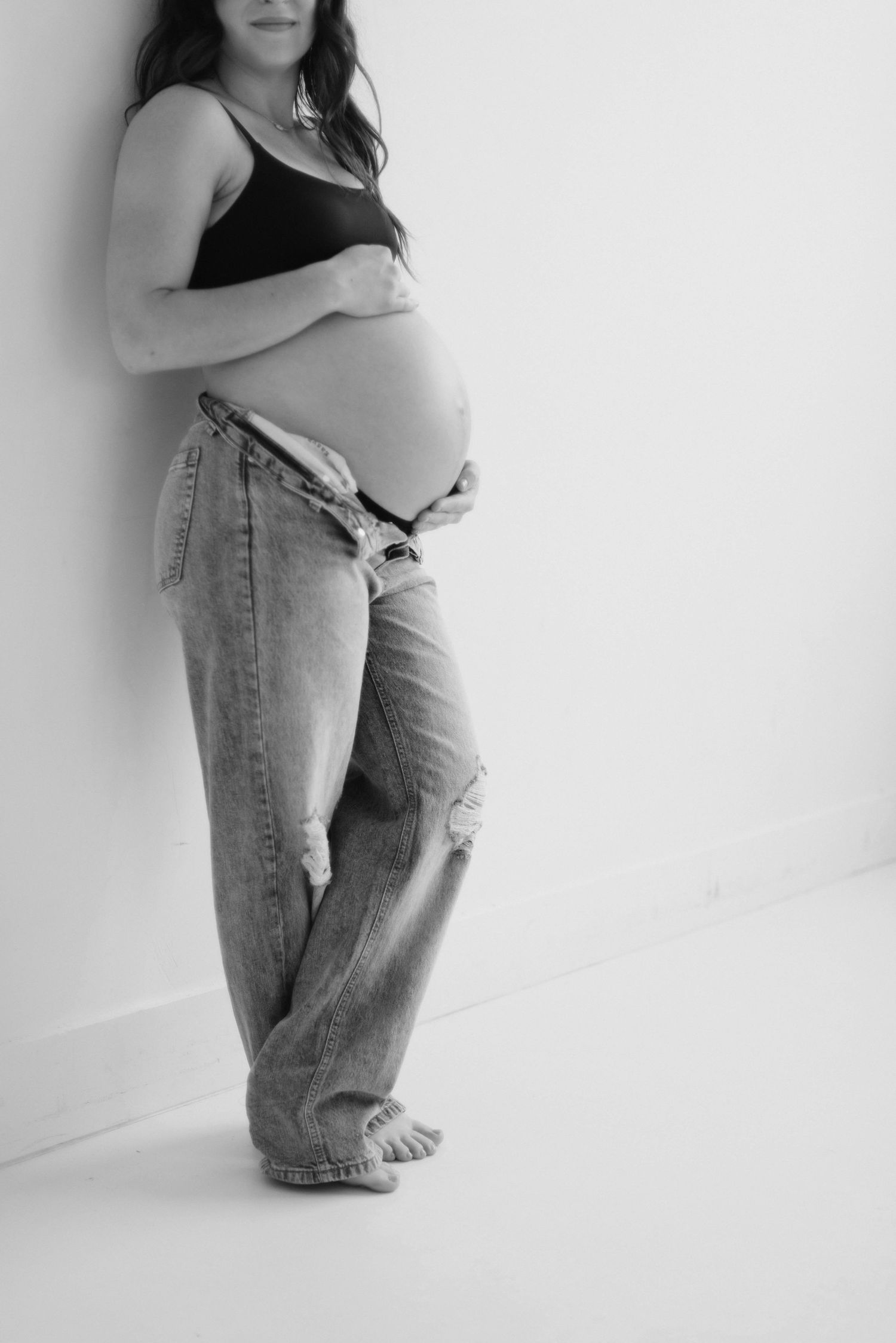Minimalist black and white maternity portraits showing profile poses against white wall.