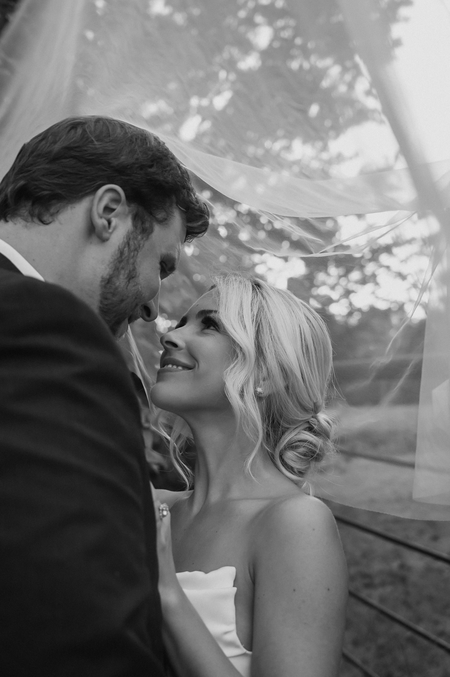 Black and white wedding portrait captures romantic moment between bride and groom under veil.