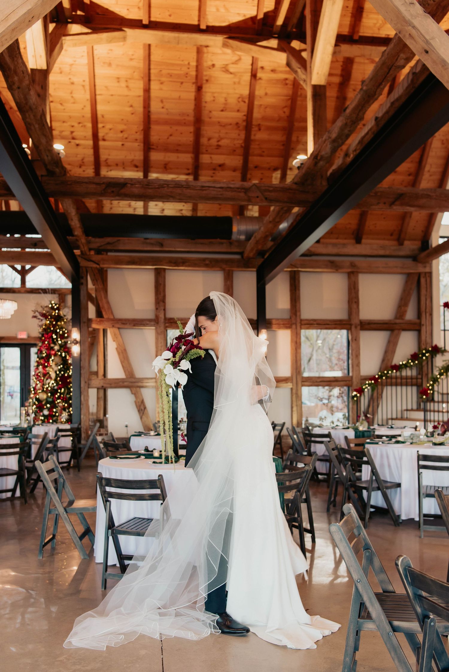Wedding couple sharing intimate moment in rustic wooden barn venue with Christmas decorations.