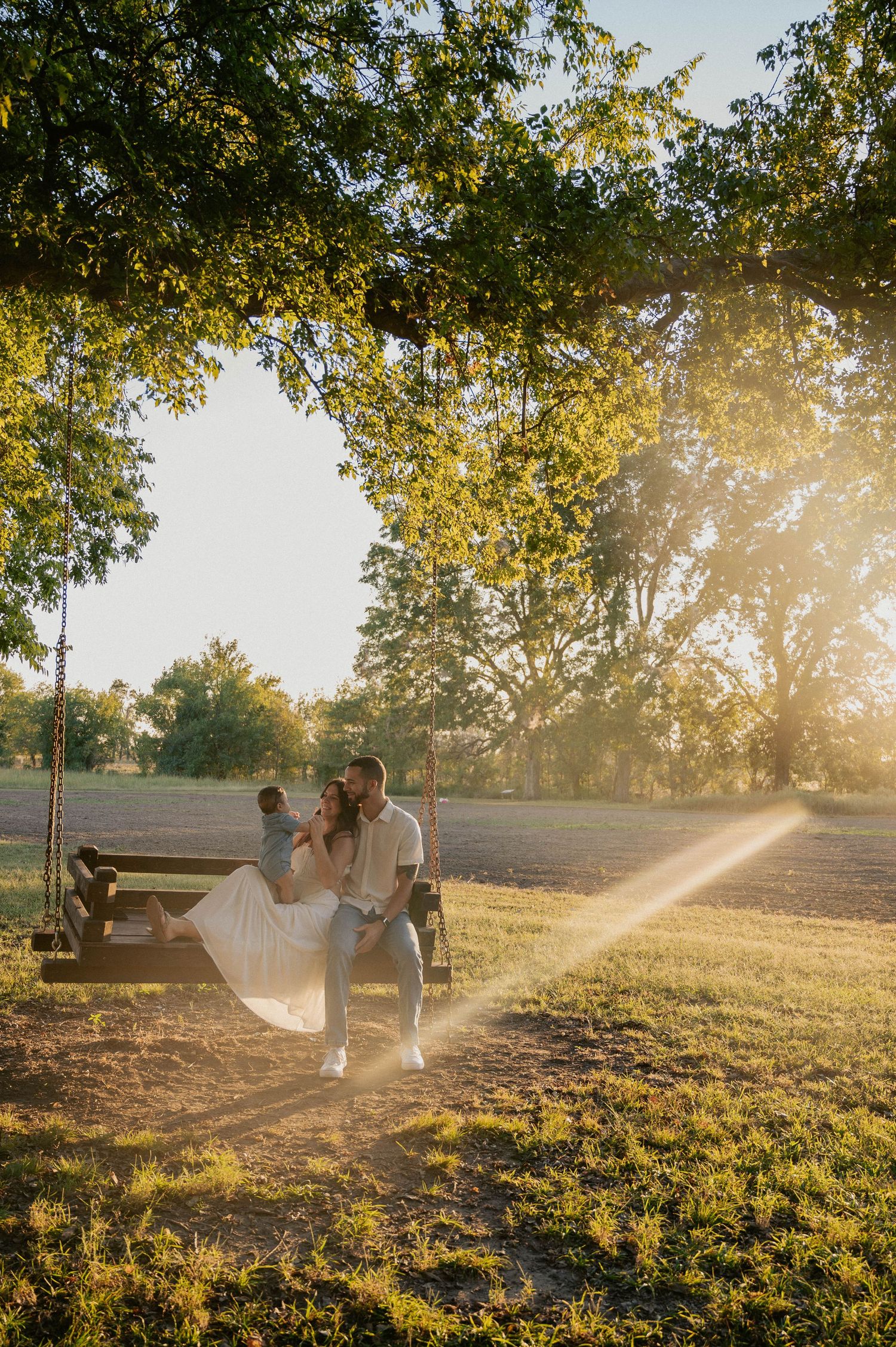 Wedding couple photographed in golden sunlight through trees at sunset.