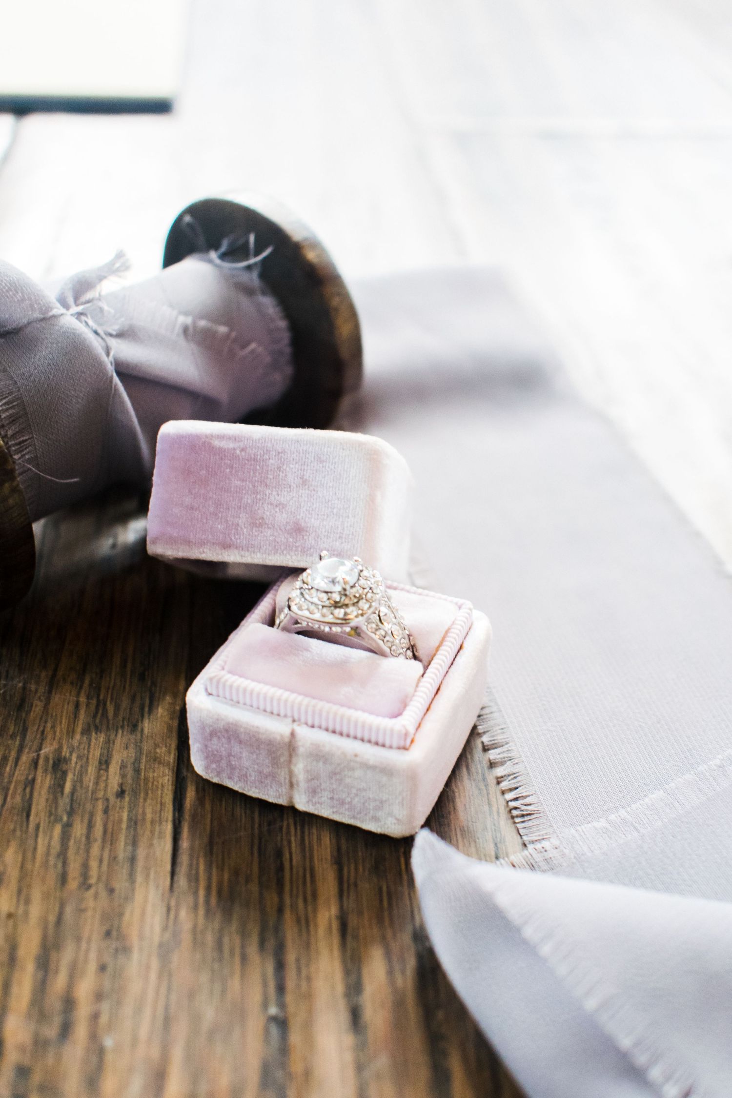 Diamond engagement ring in pink velvet box on rustic wooden surface.