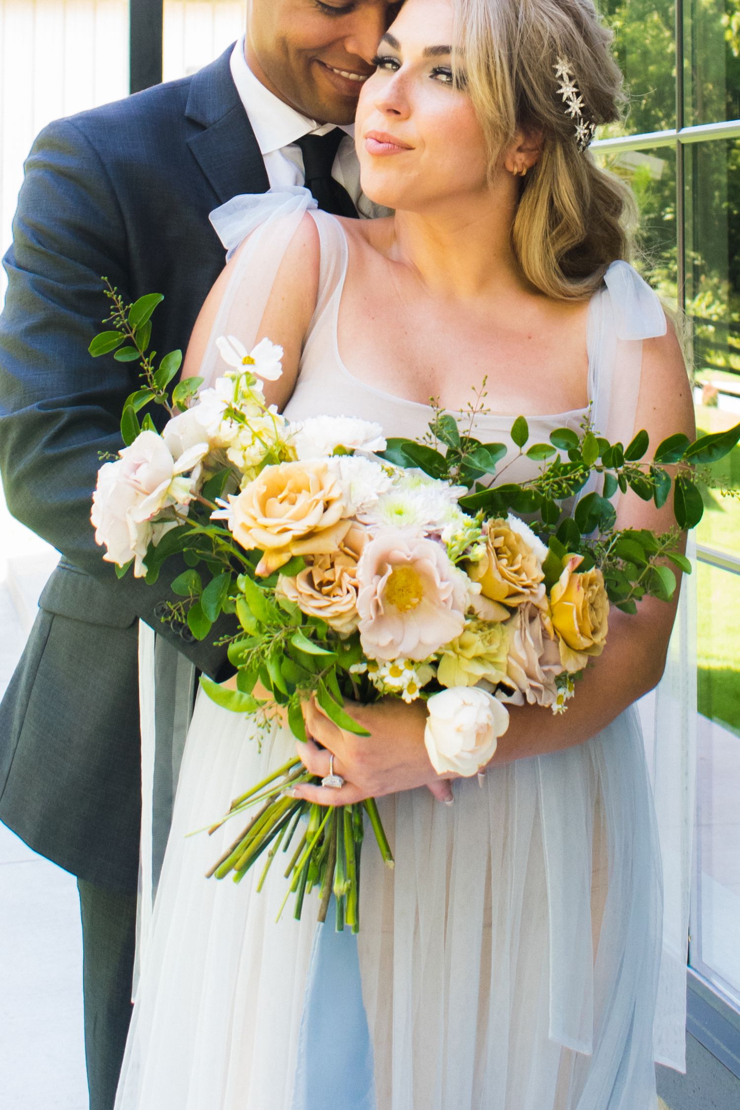 Wedding couple holding beautiful bouquet of yellow and white roses with greenery.