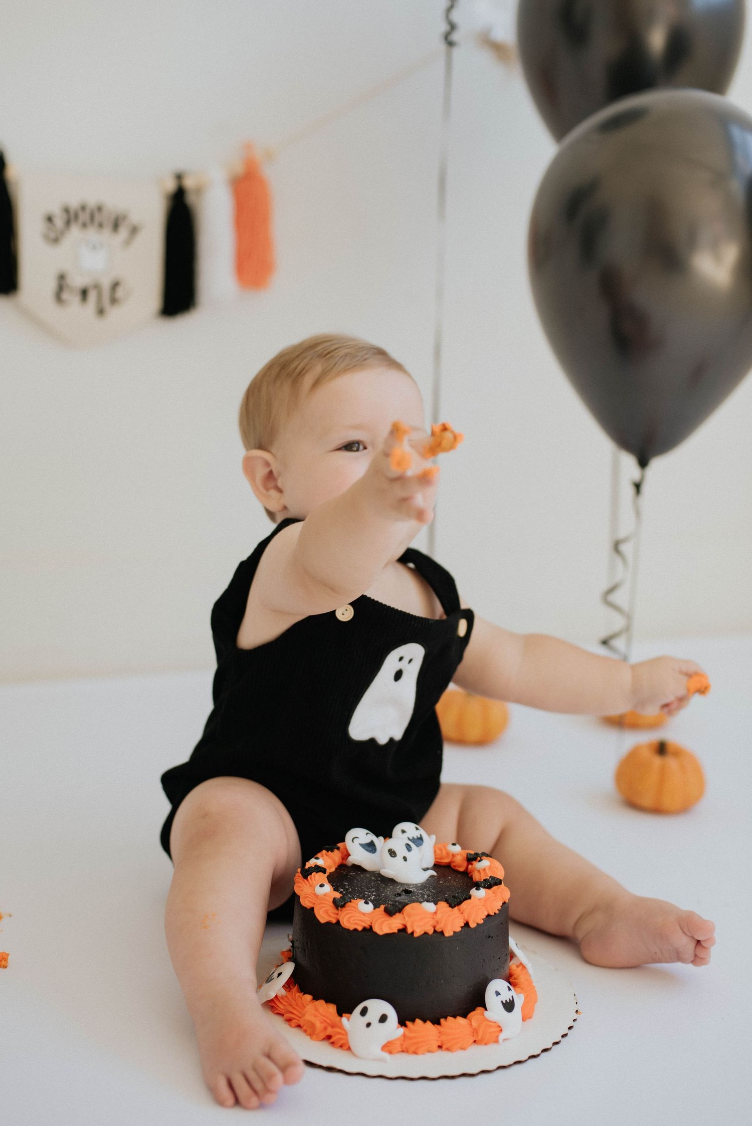 Halloween themed smash cake with ghost decorations and black balloons for a festive celebration.
