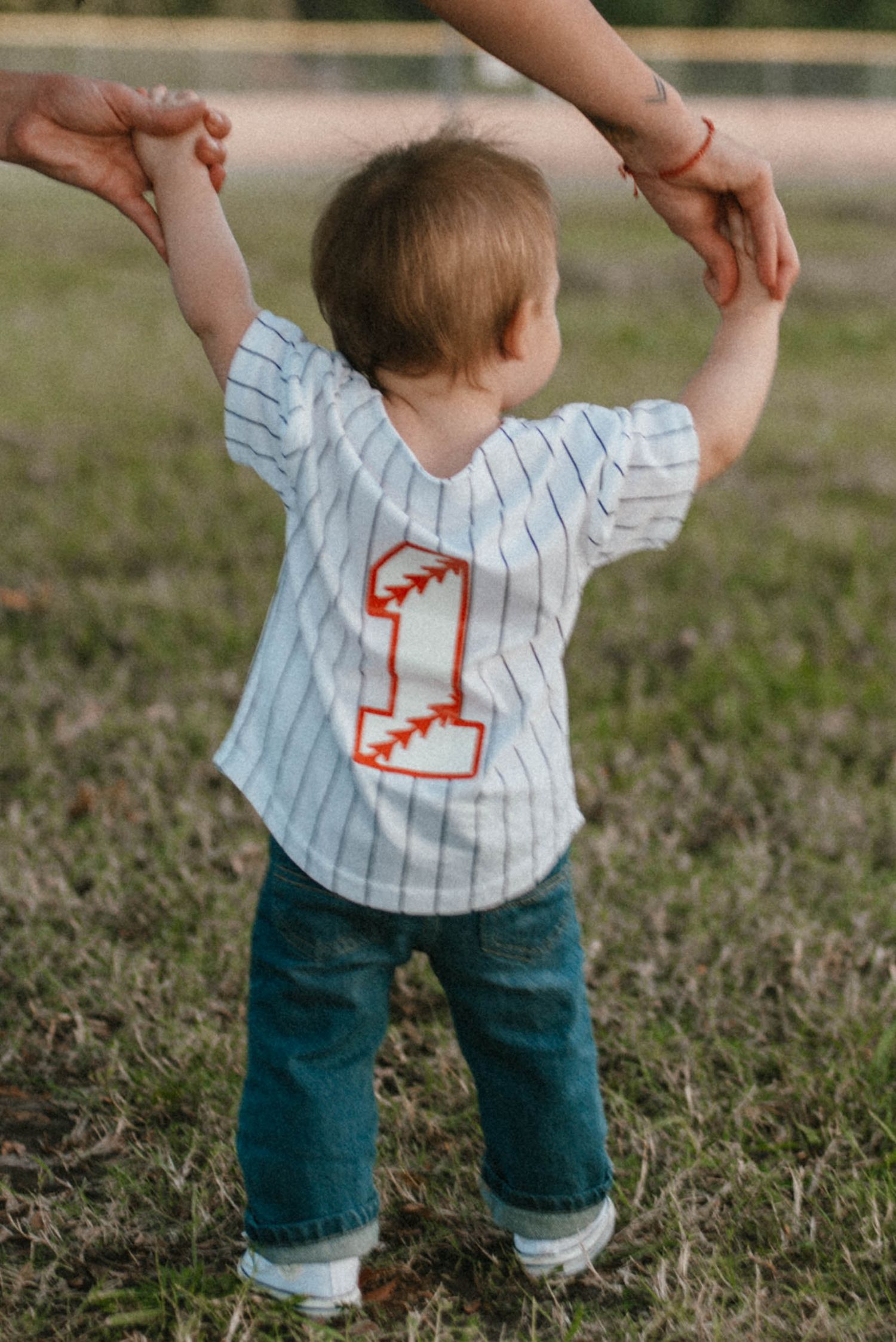 Small child in striped shirt and jeans learning to walk on grass.