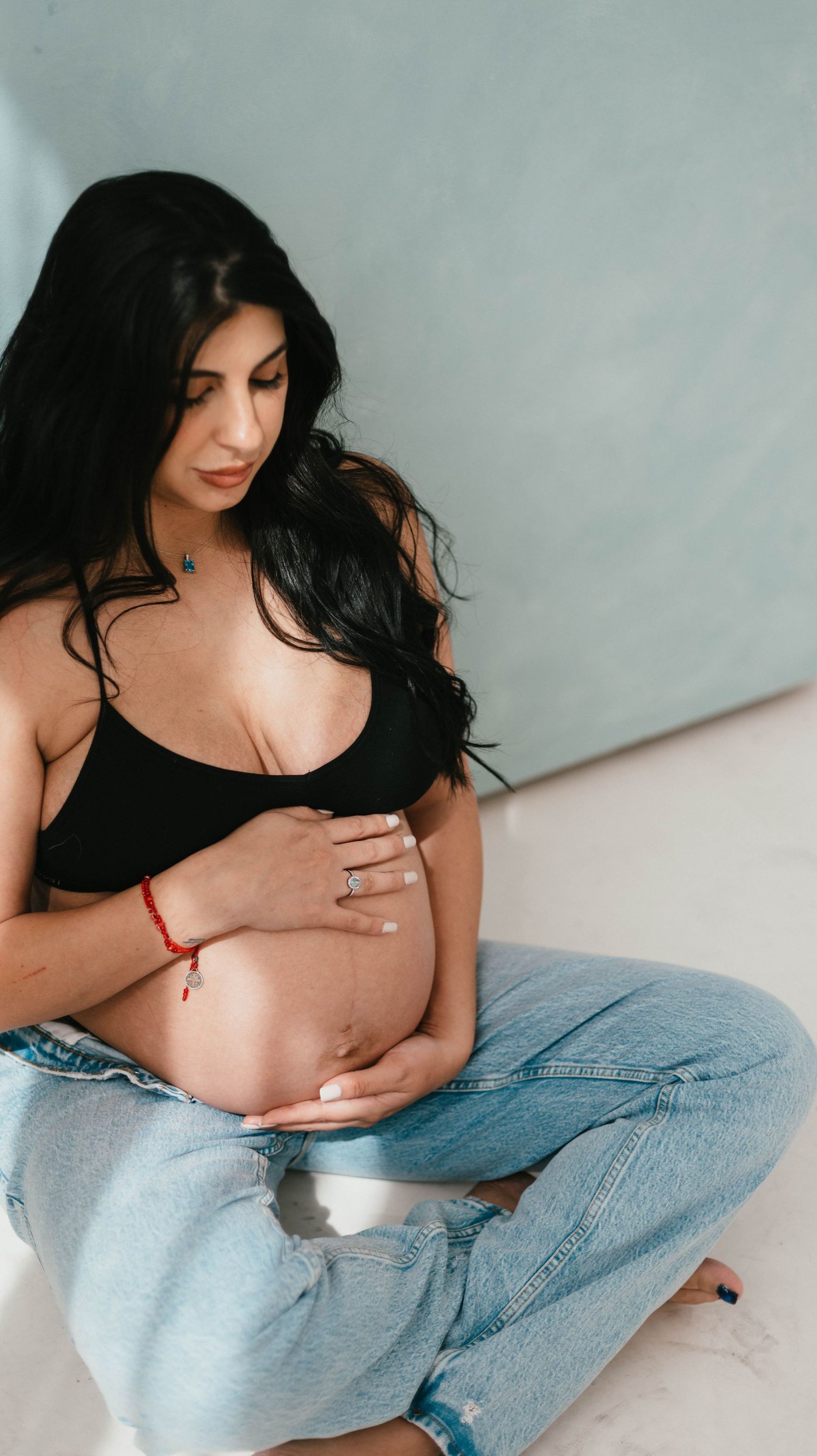 Maternity photoshoot featuring woman in black top and jeans against white background.