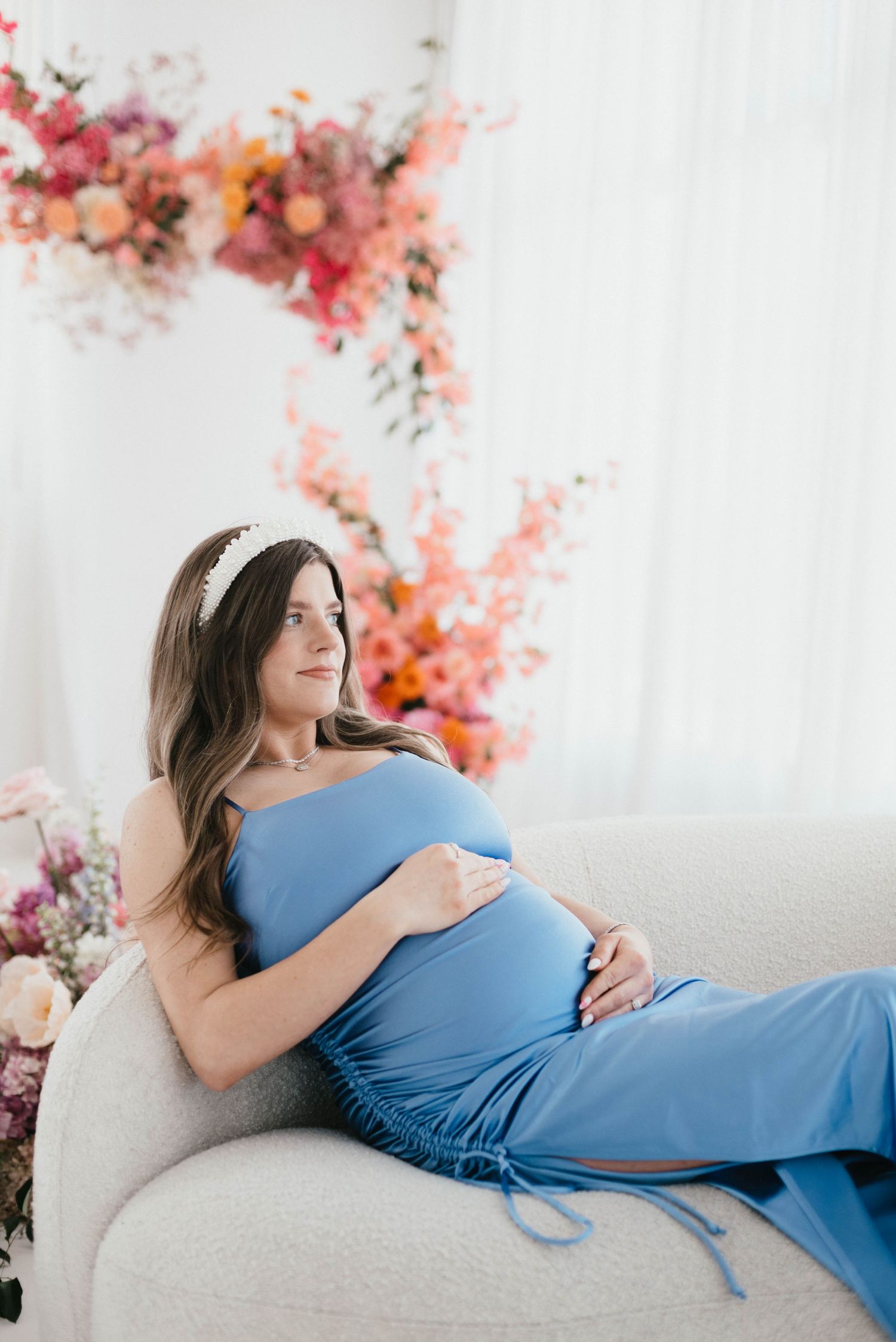 Maternity photo session with blue dress against floral backdrop.