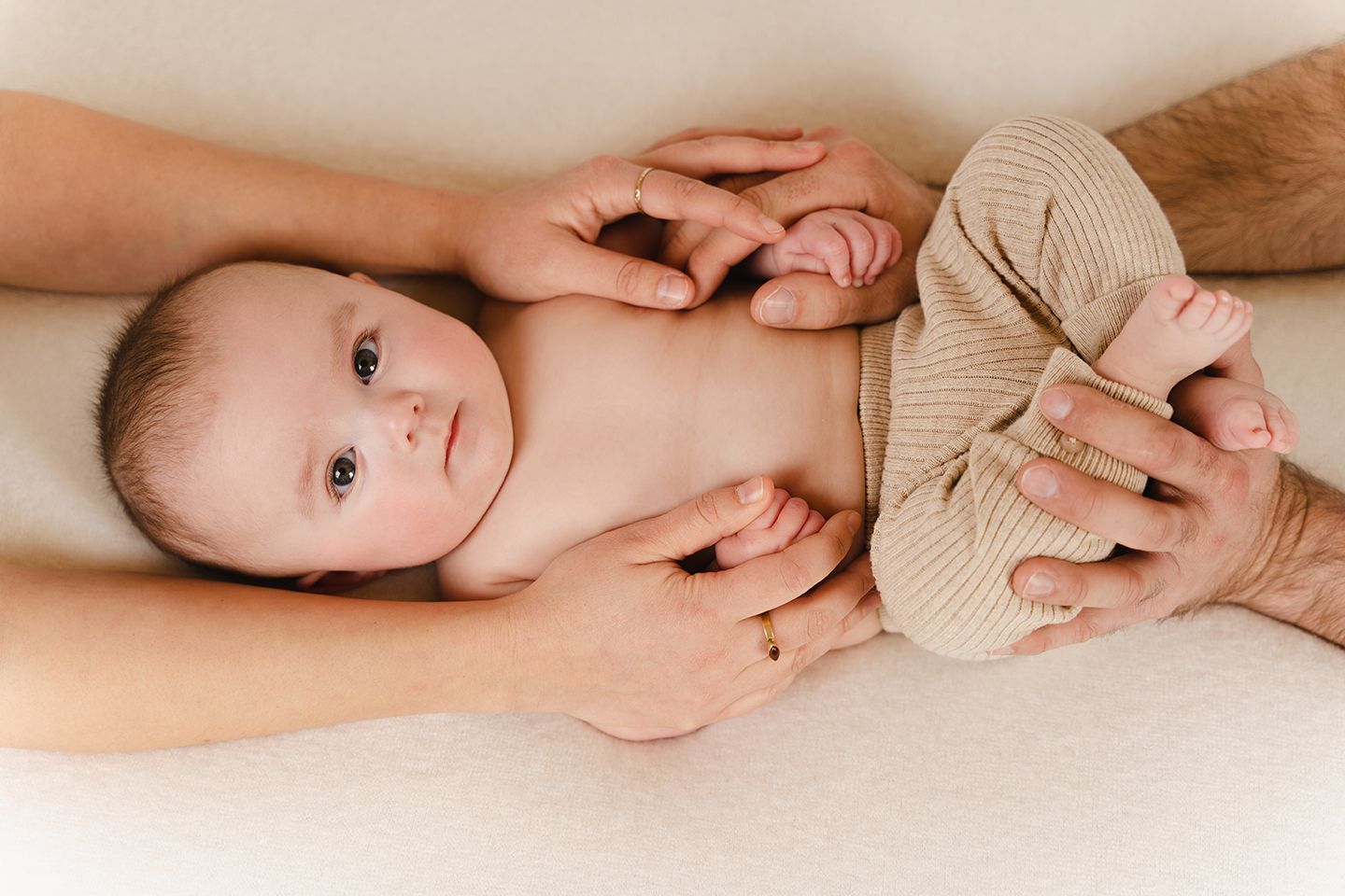 een baby van 4 maanden omringd door de armen van zijn ouders tijdens een babyreportage in studio in Zandhoven