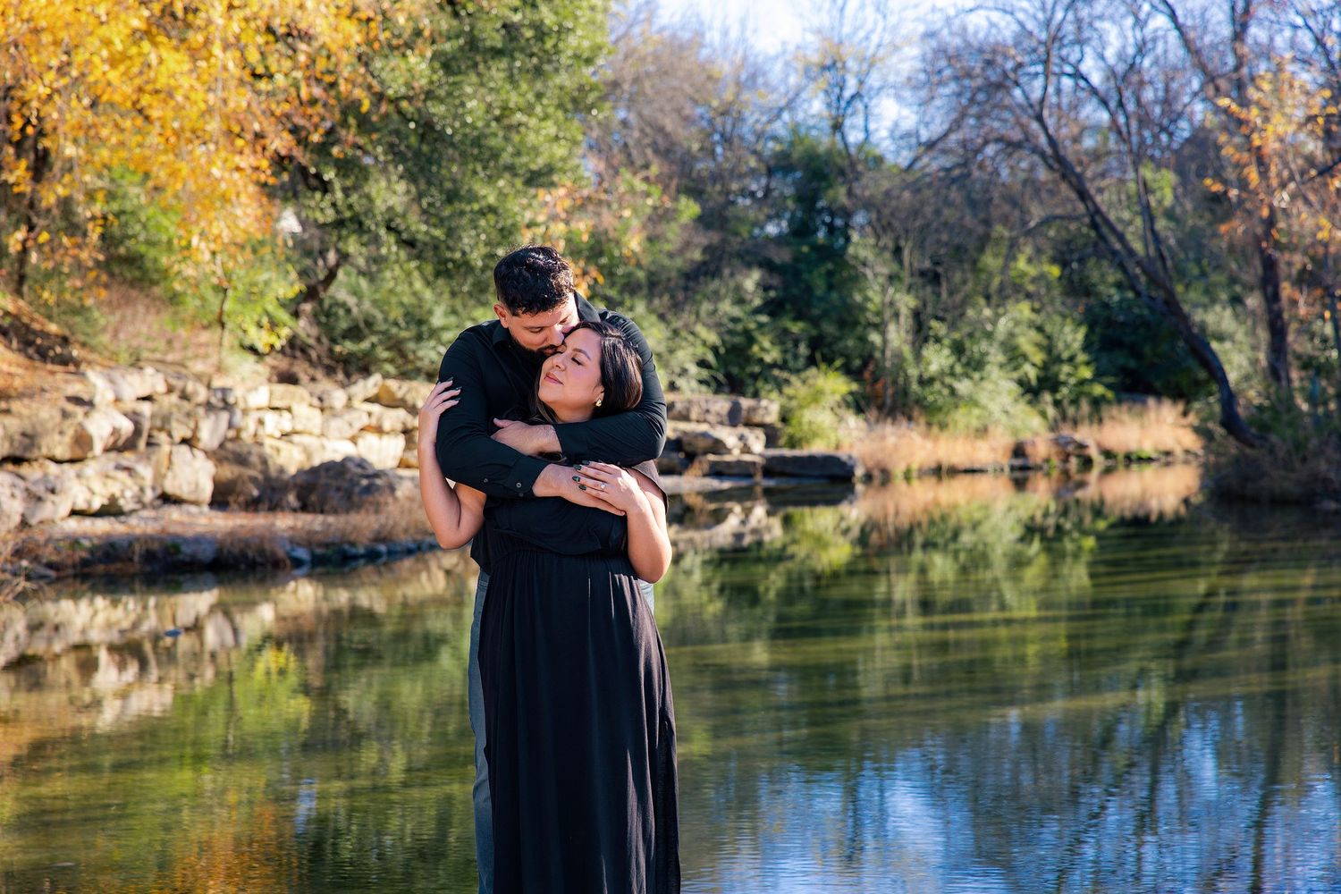 Couple embracing during a fall engagement session by a pond