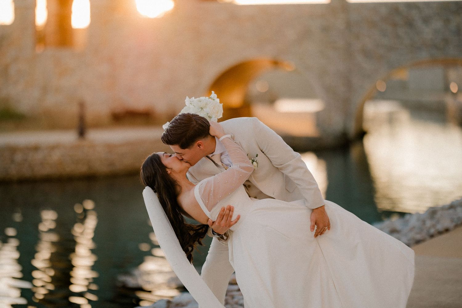 Groom dipping his bride for a kiss beside the canal at sunset