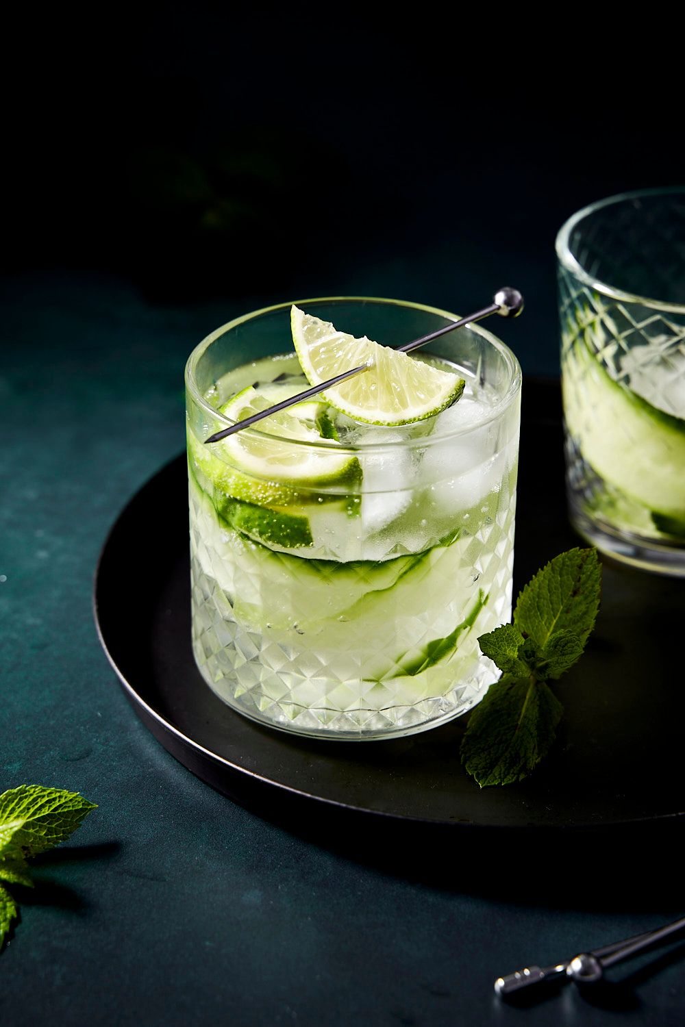 Refreshing cucumber lime cocktail with mint garnish served in crystal glasses on a dark tray.