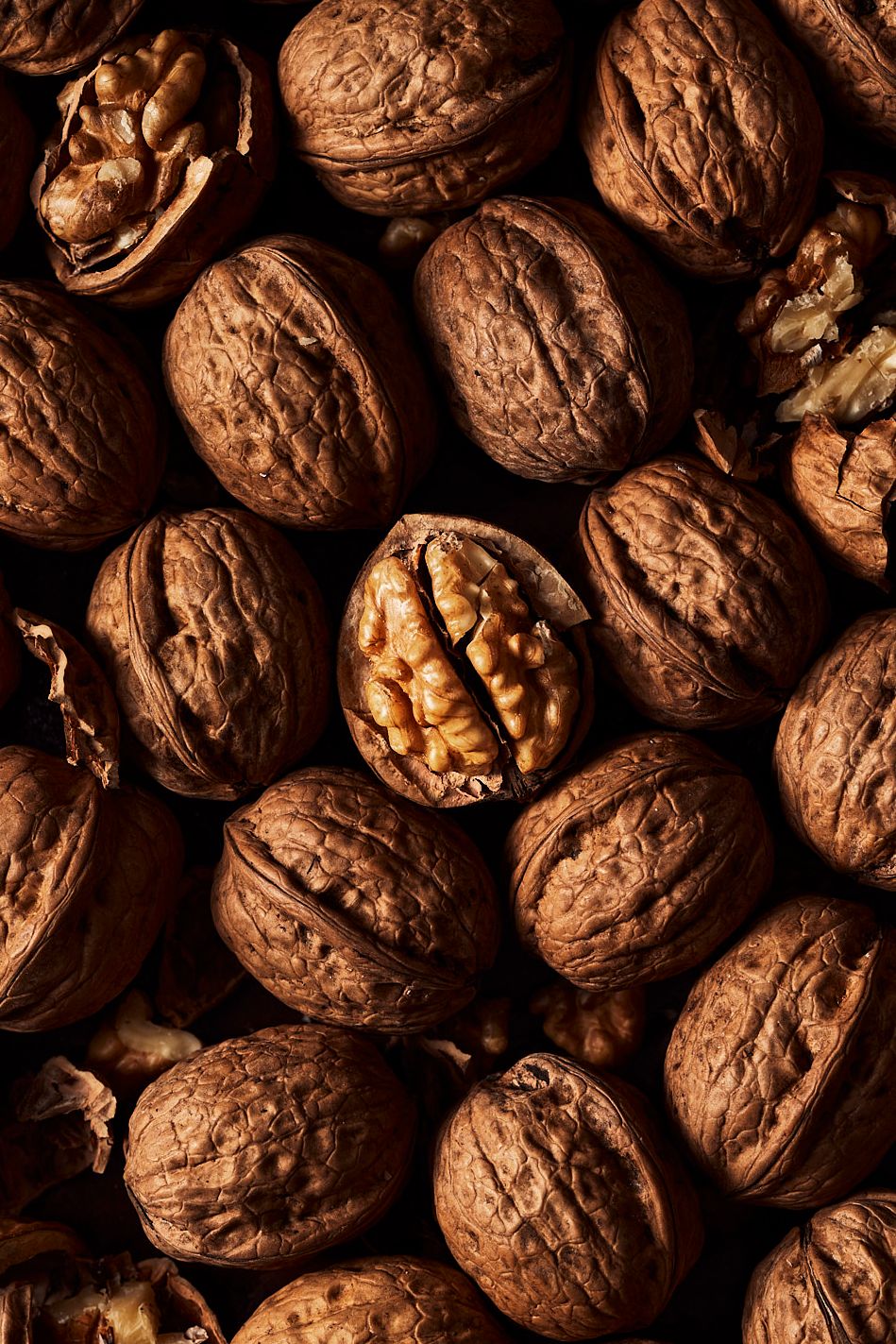 Close-up of whole walnuts with one cracked open revealing the nut inside, arranged as a full-frame background.