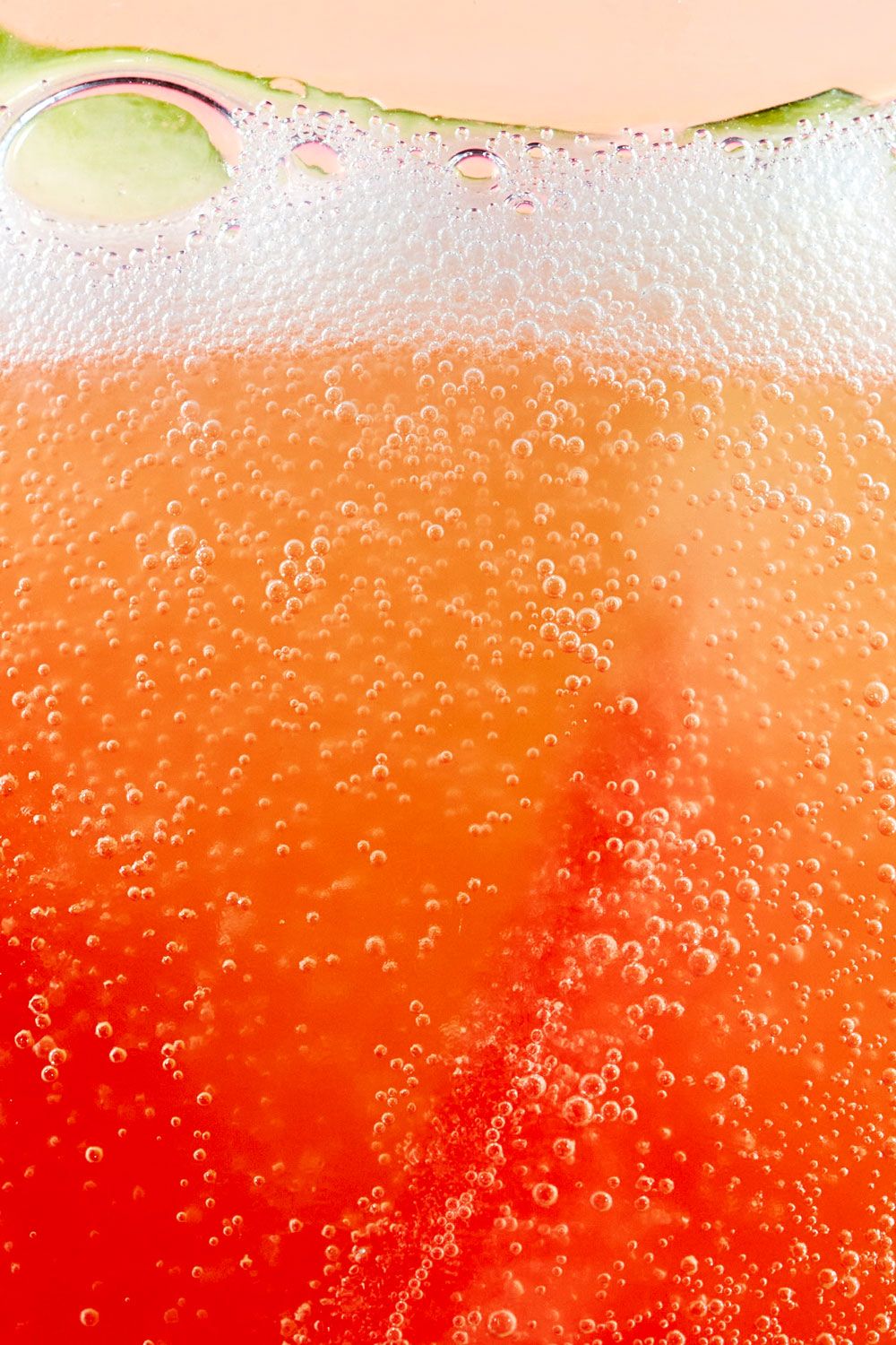 Close-up of fizzy red drink with bubbles and watermelon slice, vibrant carbonated drink texture background.